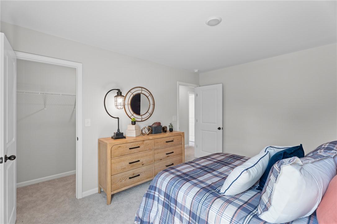 Bright bedroom with plaid bedding, wooden dresser, and walk-in closet in Davidson Homes The Stella B, Opelika, Alabama
