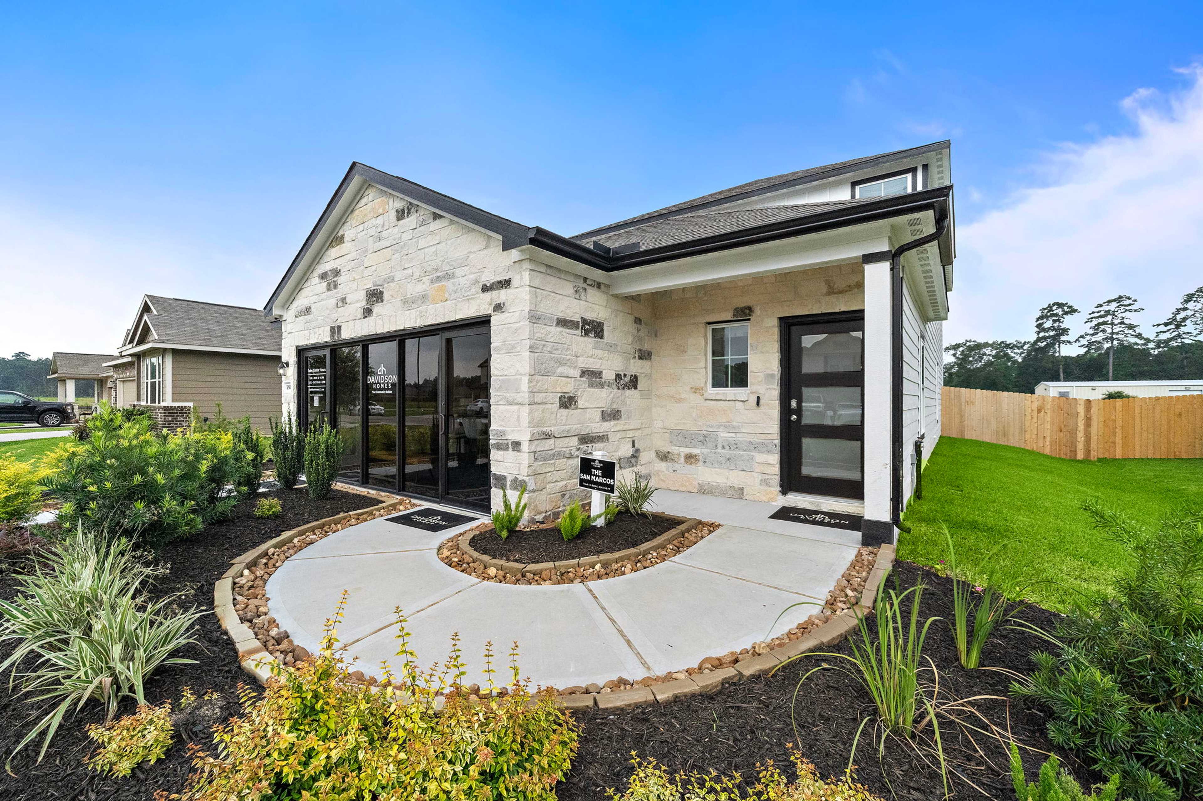 Stone facade home exterior at Liberty Estates in Cleveland Texas with large glass doors, covered entry, and lush landscaping