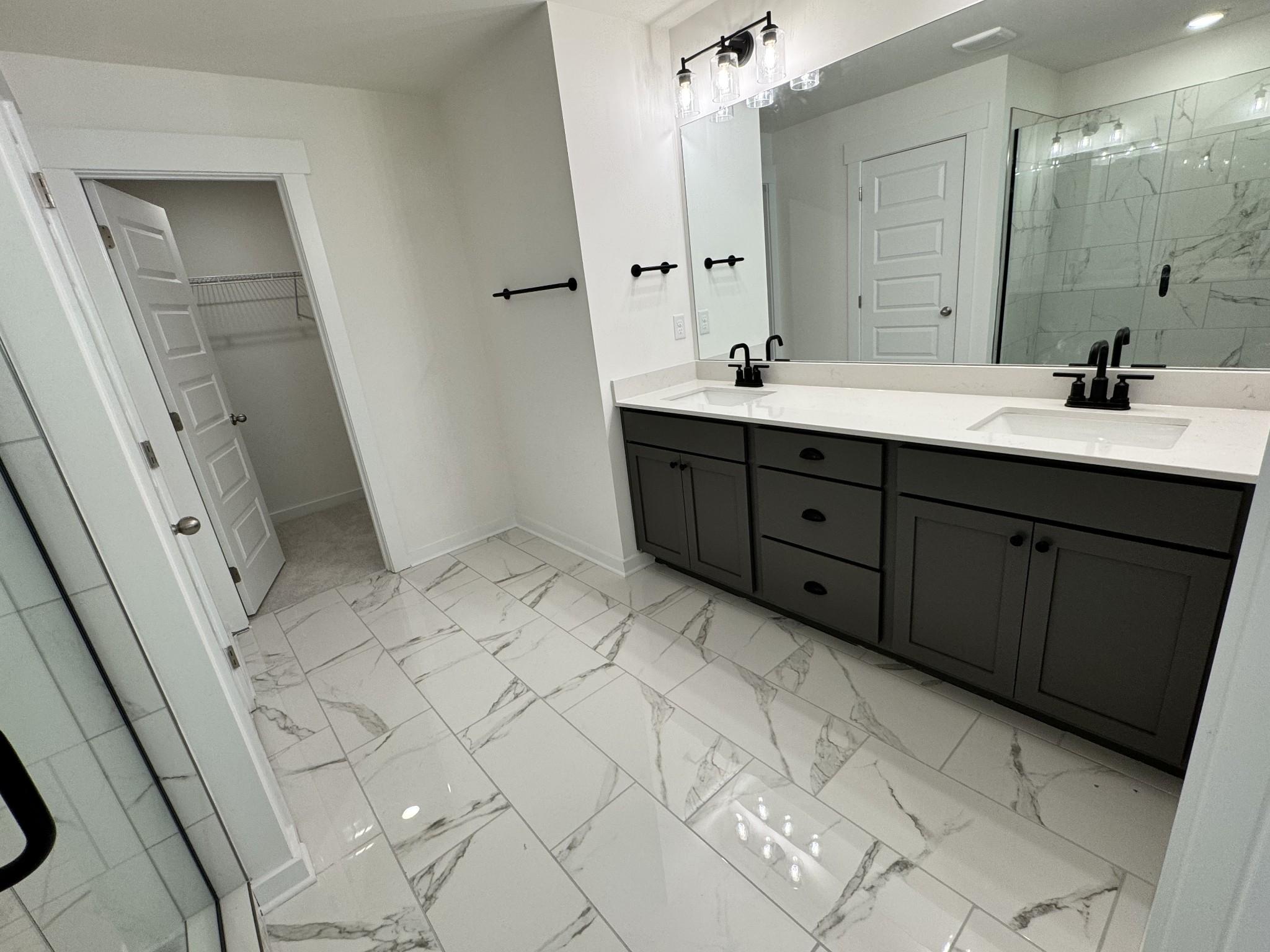 Modern master bath with double vanity, dark shaker cabinets, white quartz counters, black faucets, glass shower, and walk-in closet in Davidson Homes The Willow, Gallatin TN