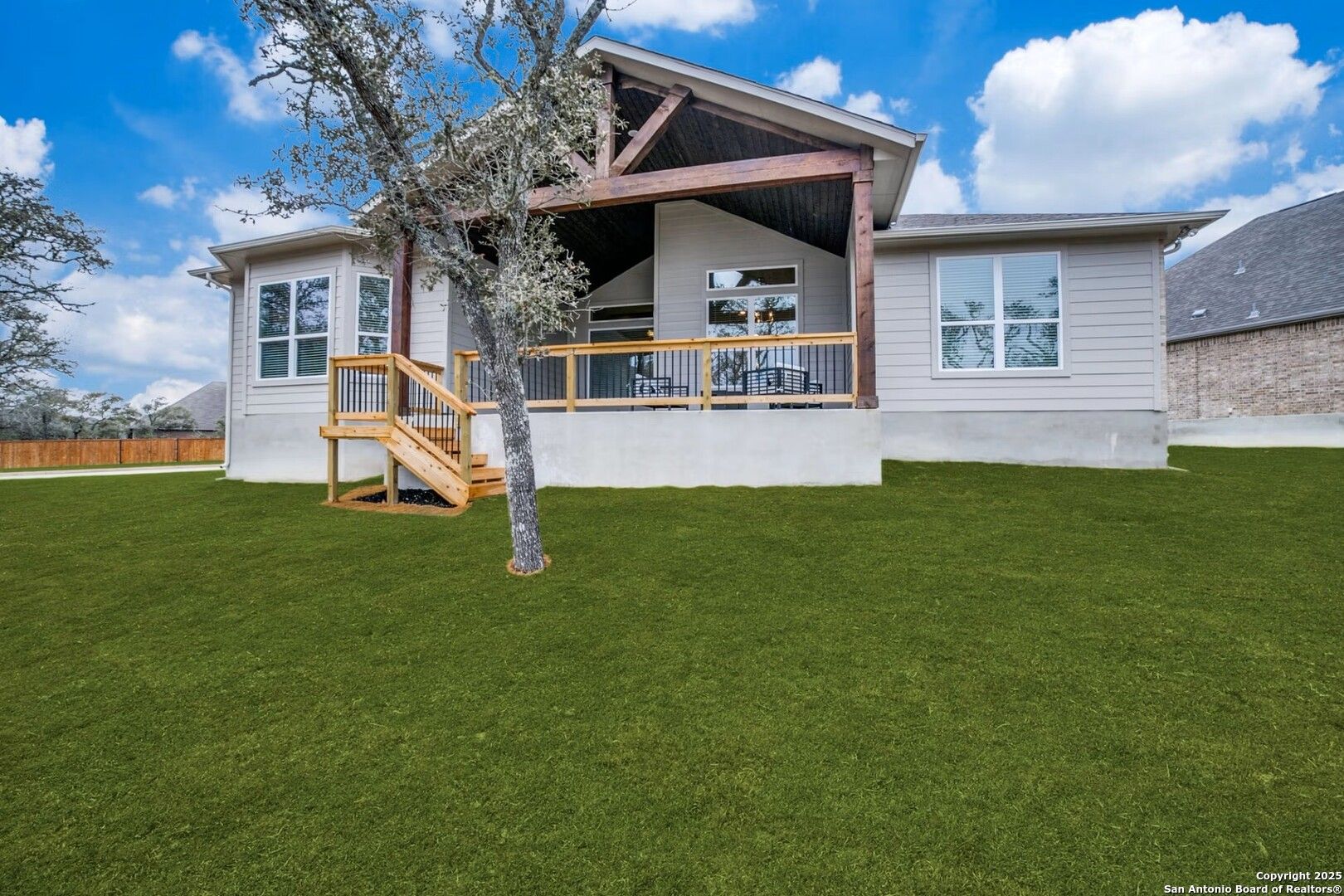 Covered patio with wooden beams, stairs, and oak tree in lush backyard of The Garner B by Davidson Homes, Castroville, TX