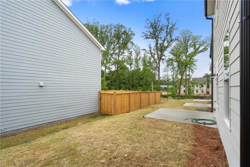 Two-story gray home side view with wooden privacy fence, grassy yard, and trees in The Village at Shallowford, Kennesaw, Georgia