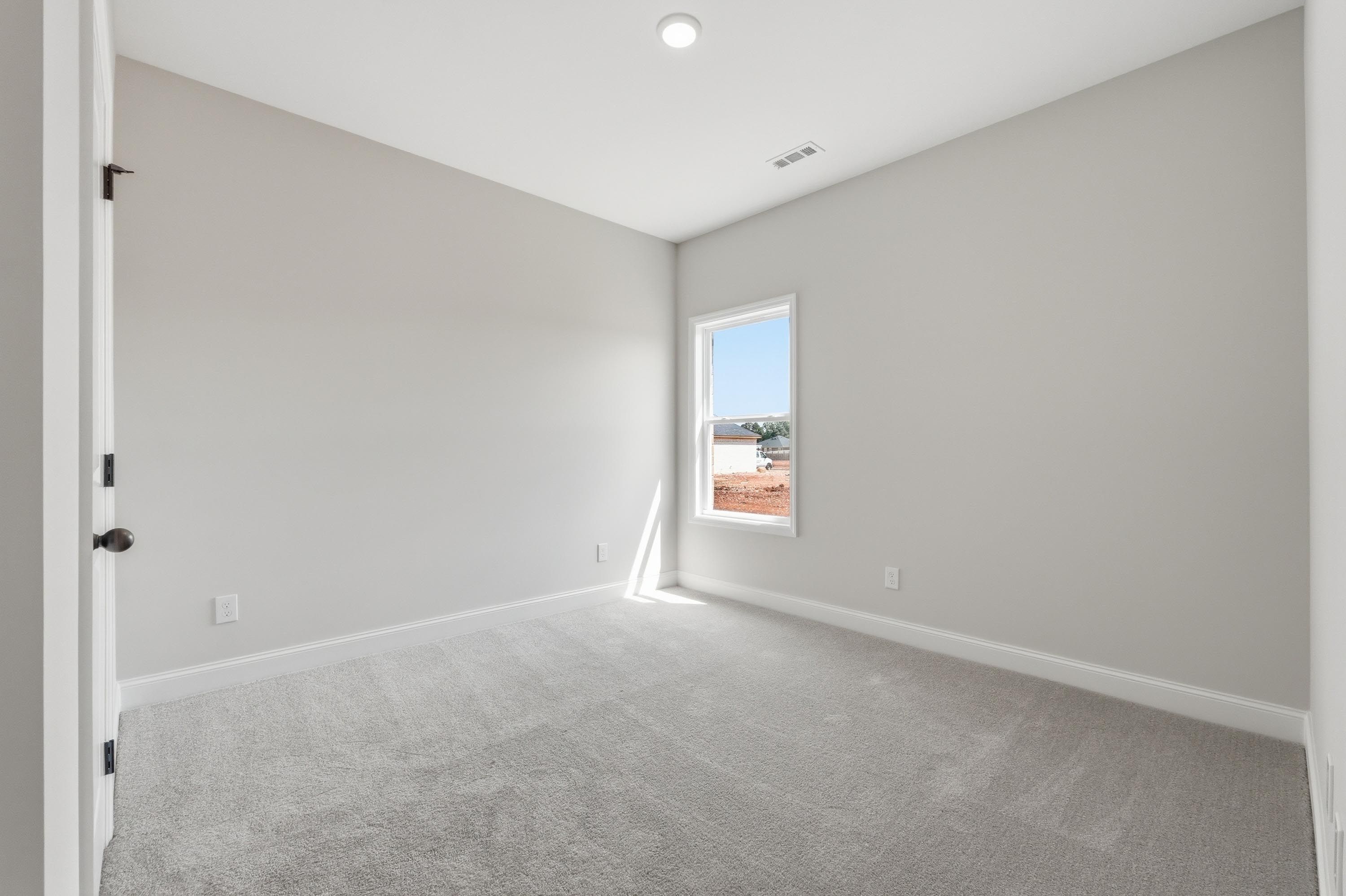Spacious bedroom in The Glen A, featuring neutral paint, plush carpeting, and natural light from a single window.