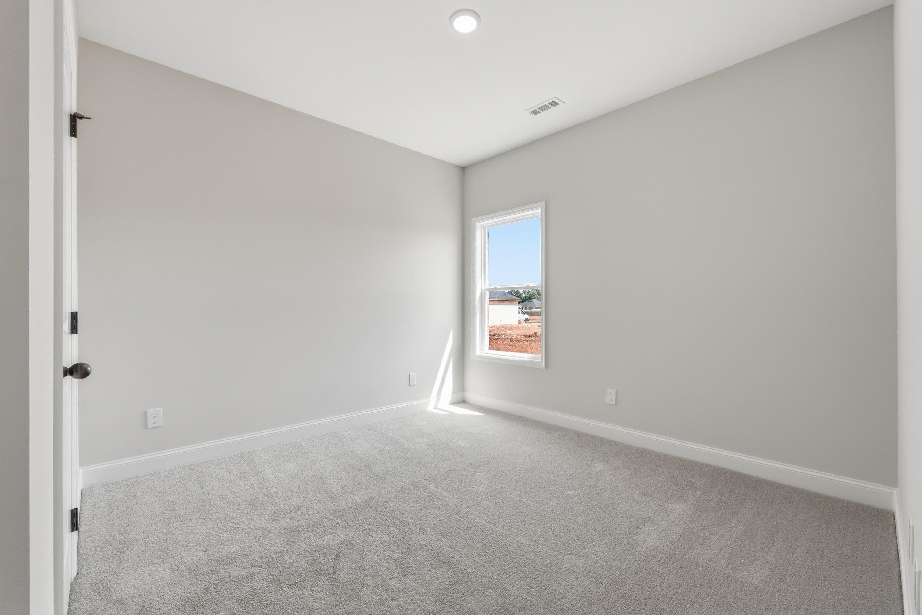 Spacious bedroom in The Glen A, featuring neutral paint, plush carpeting, and natural light from a single window.