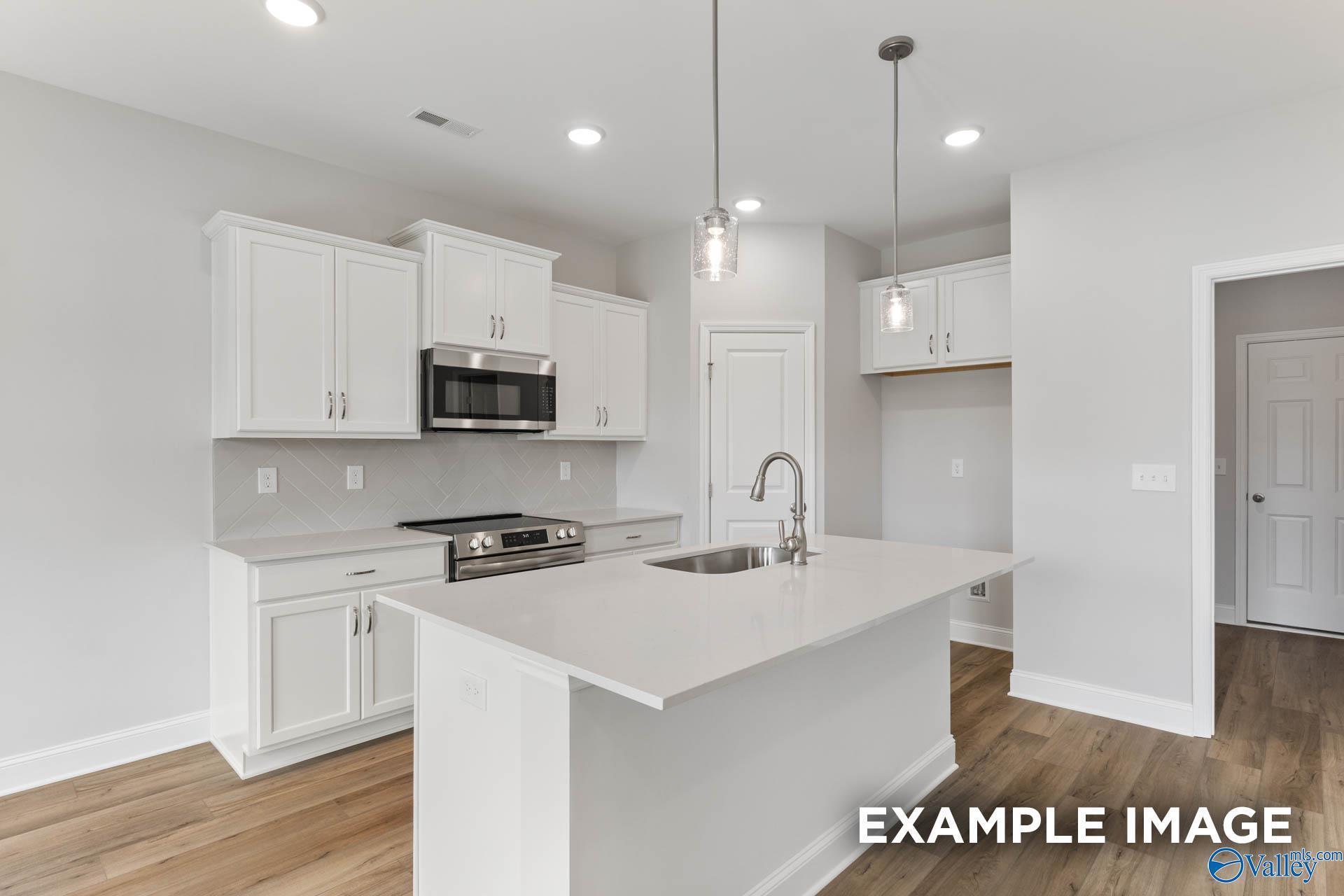 Modern kitchen with white cabinets, quartz island, and stainless appliances in The Butler floor plan, Heritage Lakes.