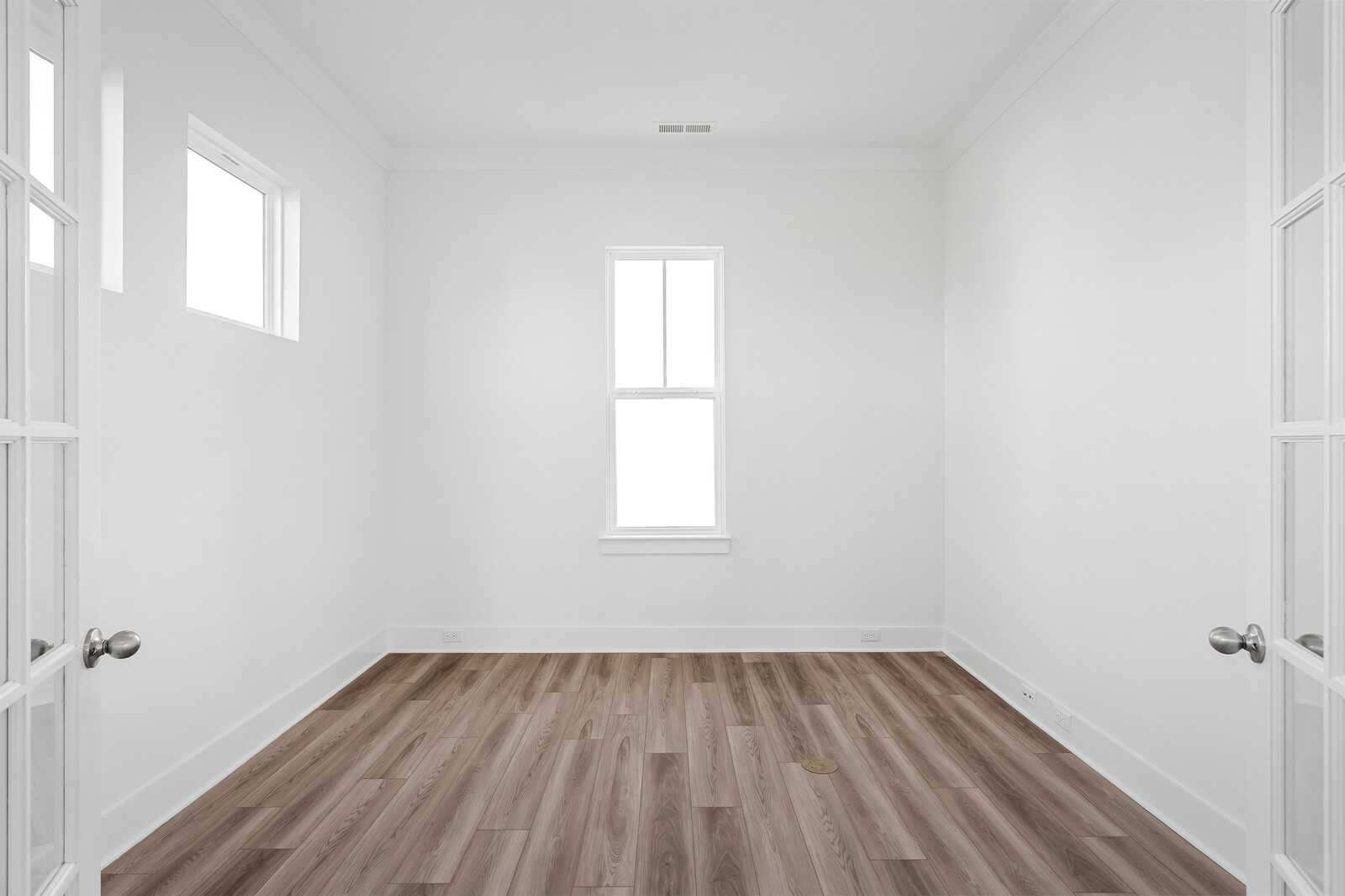 Empty bedroom with white walls, hardwood floors, large windows, and open French doors in Davidson Homes The Alston A, Murfreesboro, TN