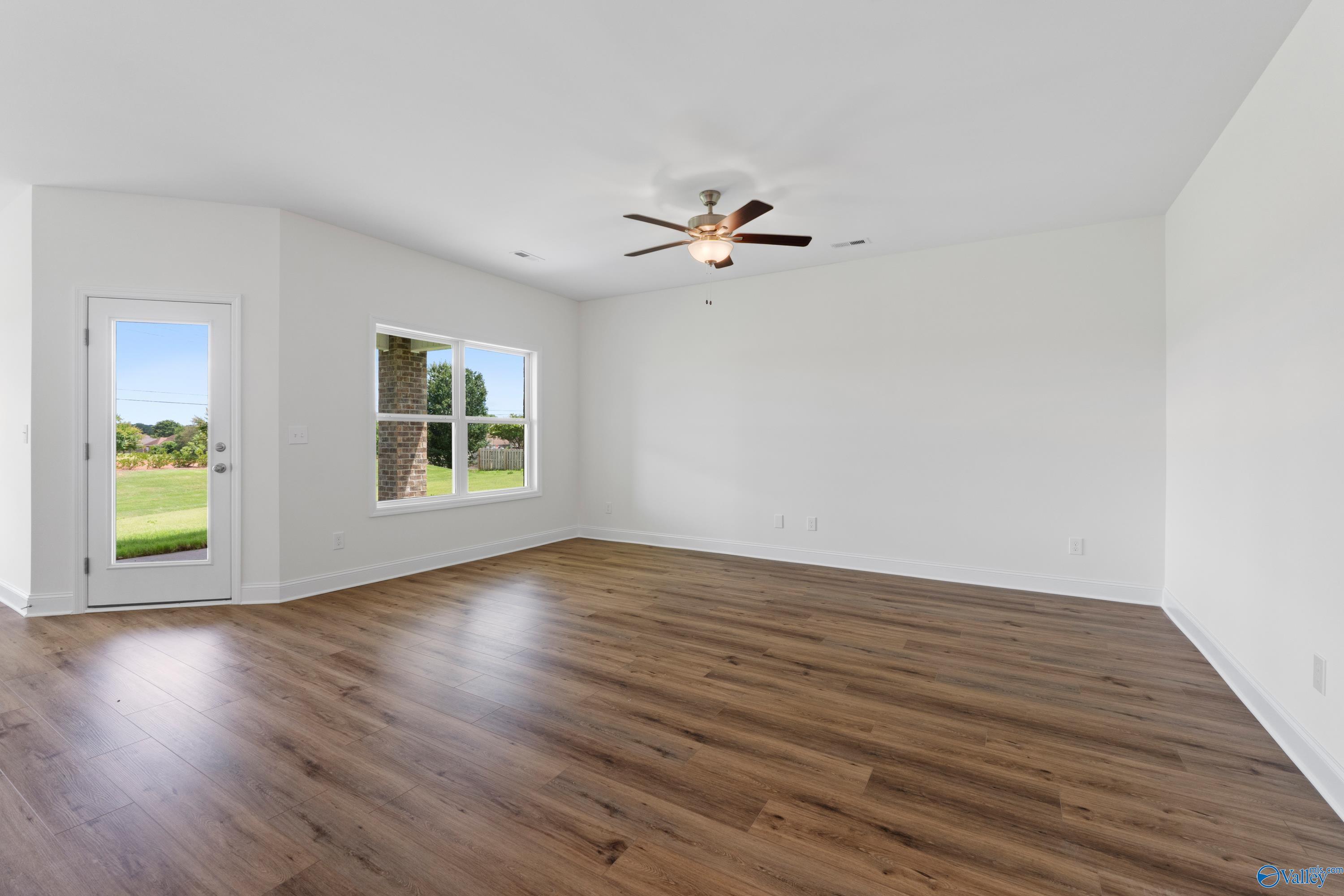Spacious living area with wood-look flooring, ceiling fan, and backyard access in The Everett B home in Athens, AL.