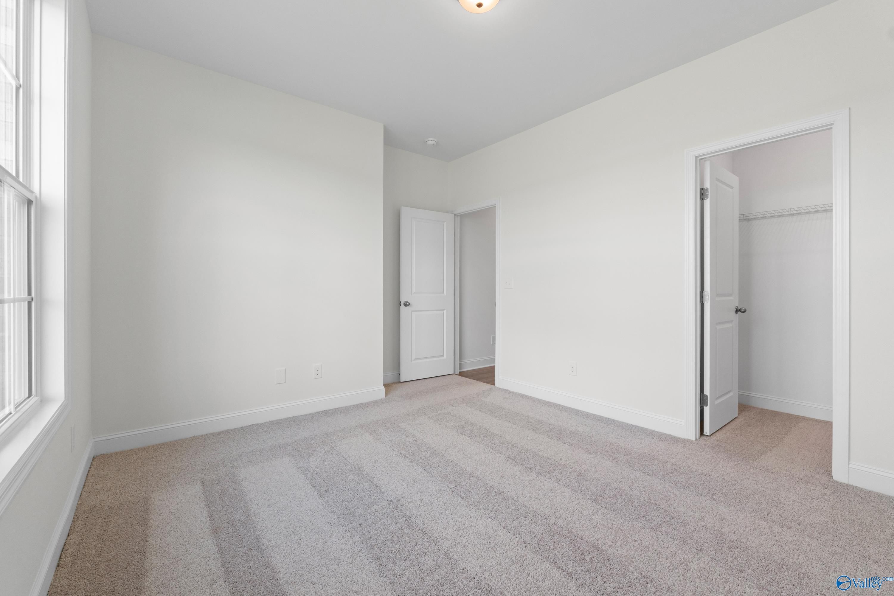 Spacious bonus room with white walls, neutral carpet, large window, and walk-in closet in Davidson Homes The Rockford B, Toney, Alabama