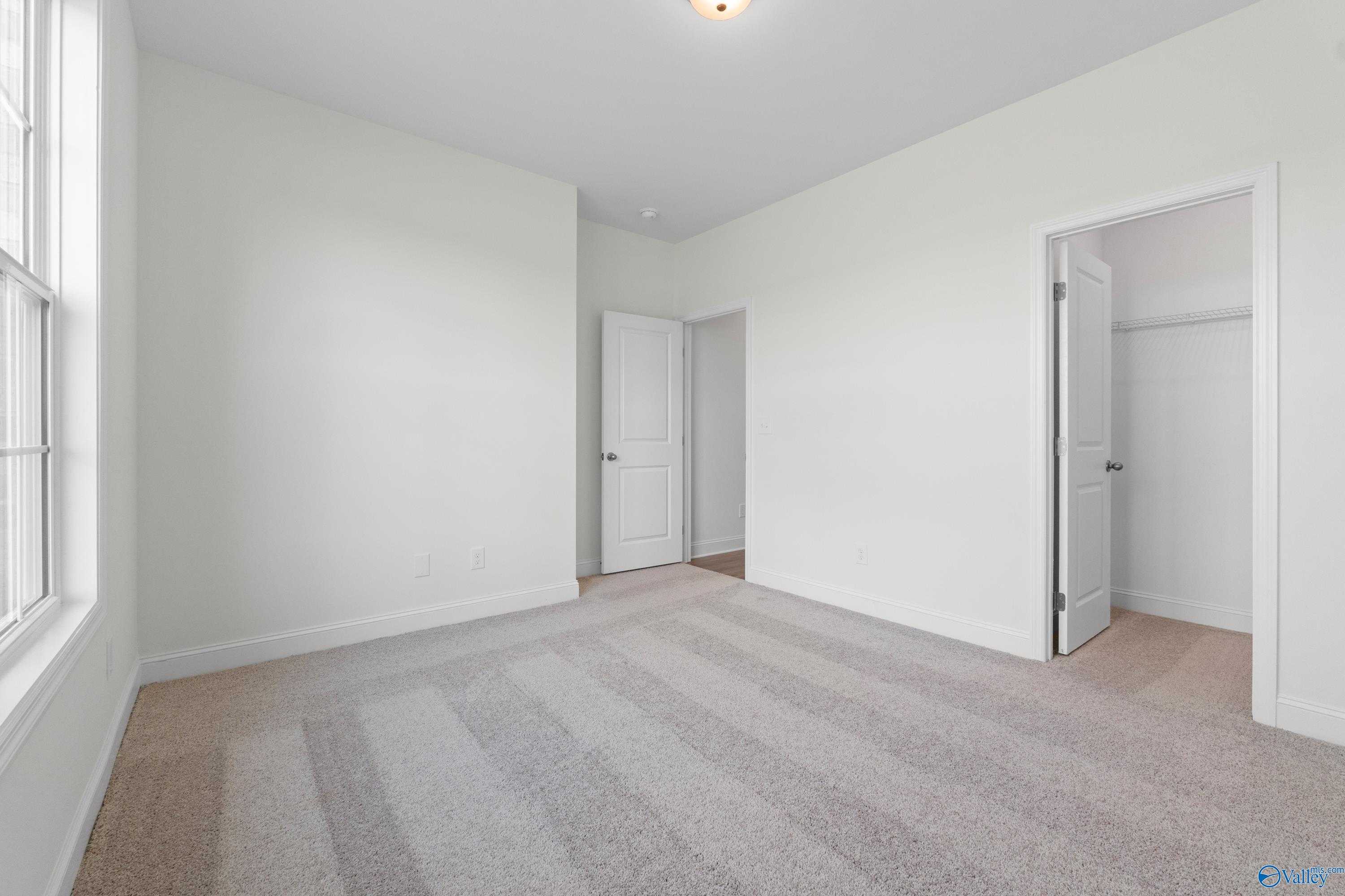 Spacious bonus room with white walls, neutral carpet, large window, and walk-in closet in Davidson Homes The Rockford B, Toney, Alabama