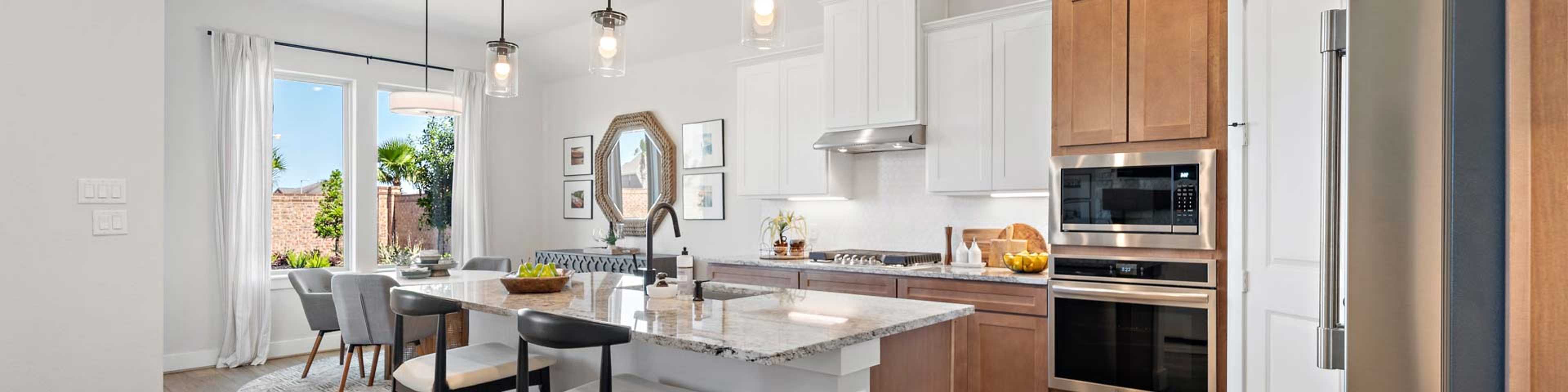 Modern open kitchen with white cabinets, quartz island, bar stools, and stainless appliances in new Rosenberg home