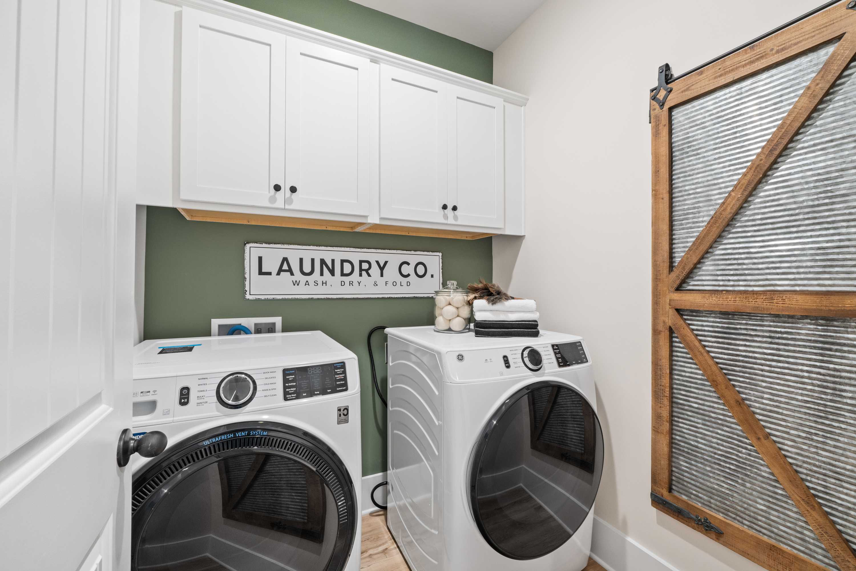 Spacious laundry room in Spragins Cove Huntsville AL with white washer dryer green accent wall white cabinets and sliding barn door