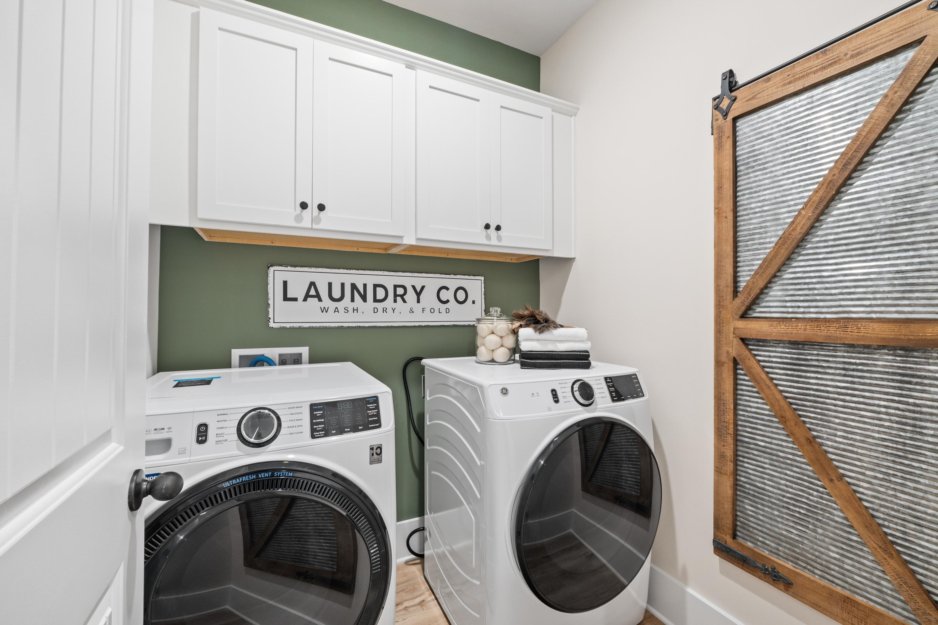 Spacious laundry room in Spragins Cove Huntsville AL with white washer dryer green accent wall white cabinets and sliding barn door