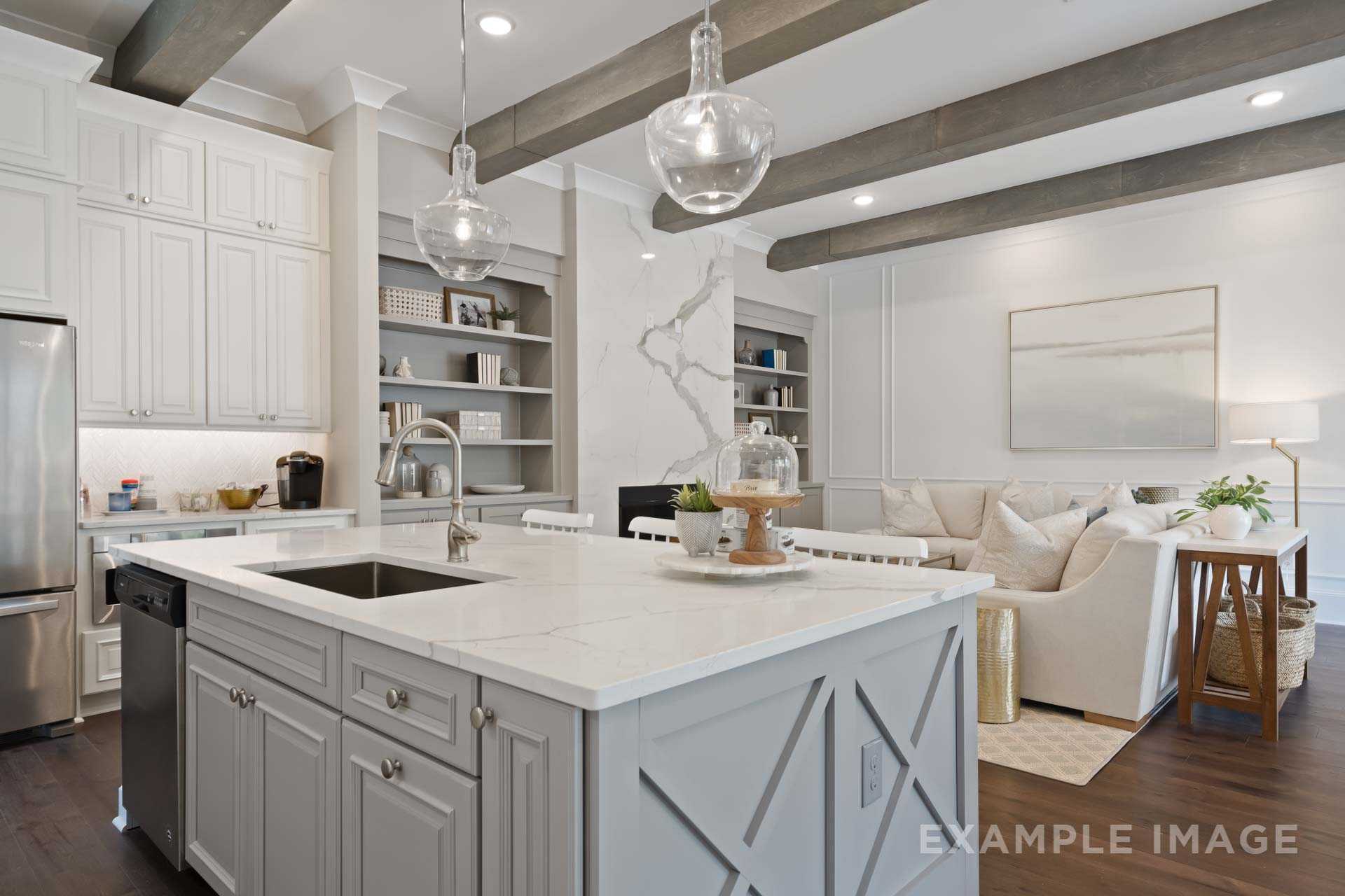 Open-concept kitchen and living area in The Seaside with white shaker cabinets, quartz island, stainless appliances, and exposed beam ceiling