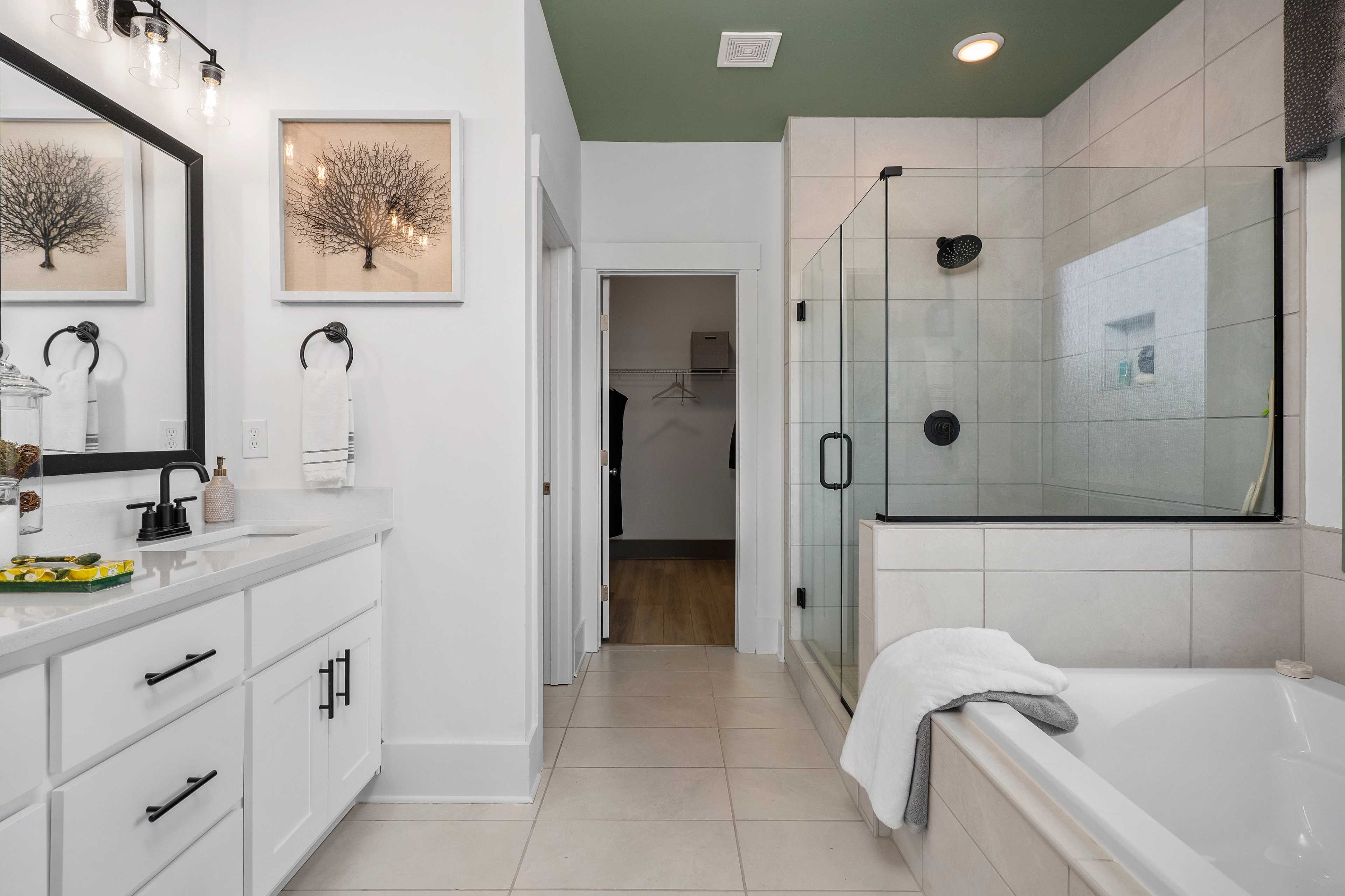 Spacious master bathroom at Barnett's Crossing in Madison AL with white vanity, glass shower, freestanding tub, and sage green ceiling