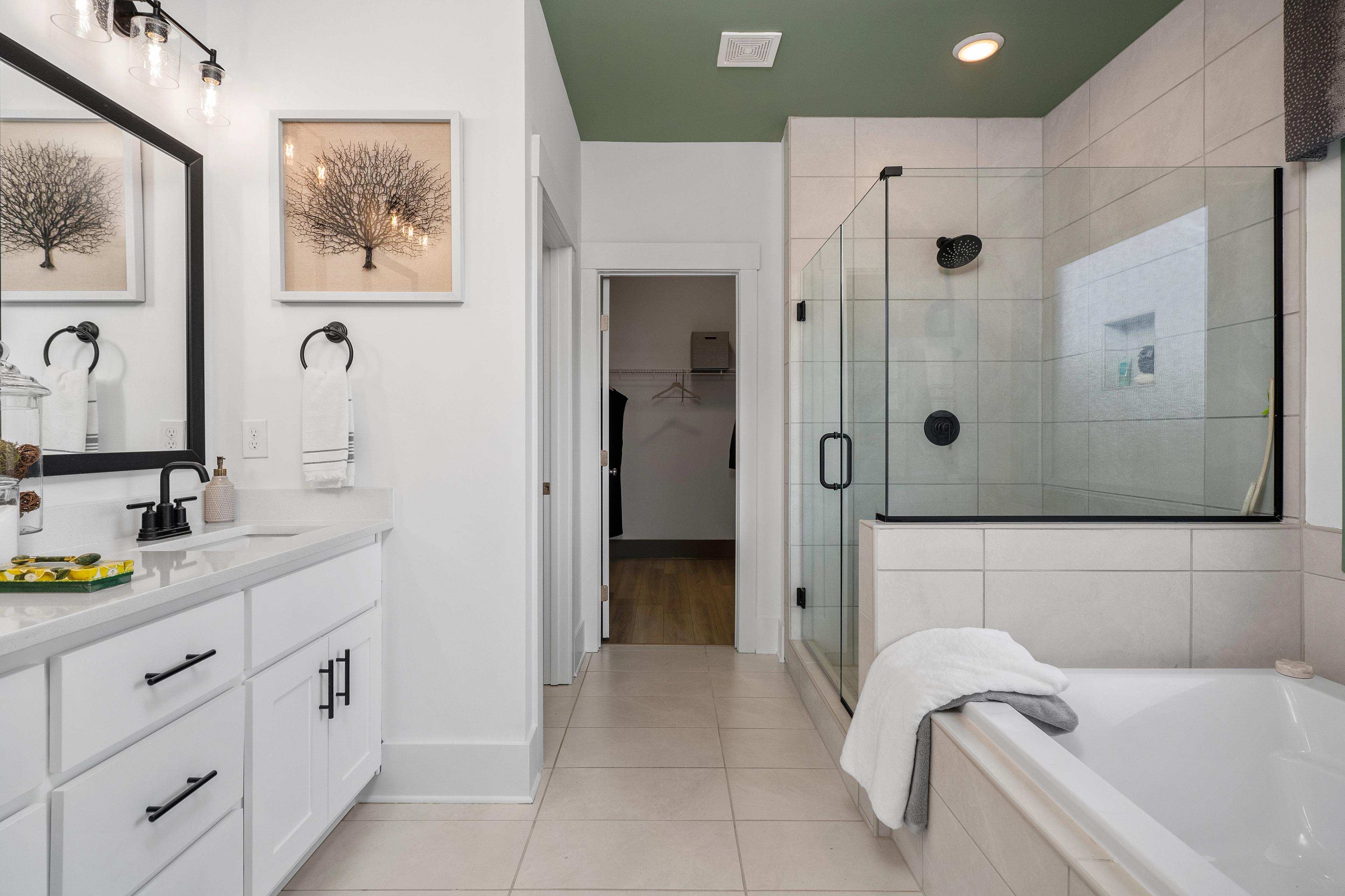 Spacious master bathroom at Barnett's Crossing in Madison AL with white vanity, glass shower, freestanding tub, and sage green ceiling