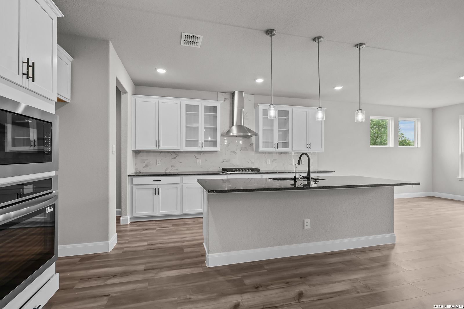 Modern white kitchen with stainless appliances, marble backsplash, granite island in Davidson Homes The Belmont H, Castroville, TX