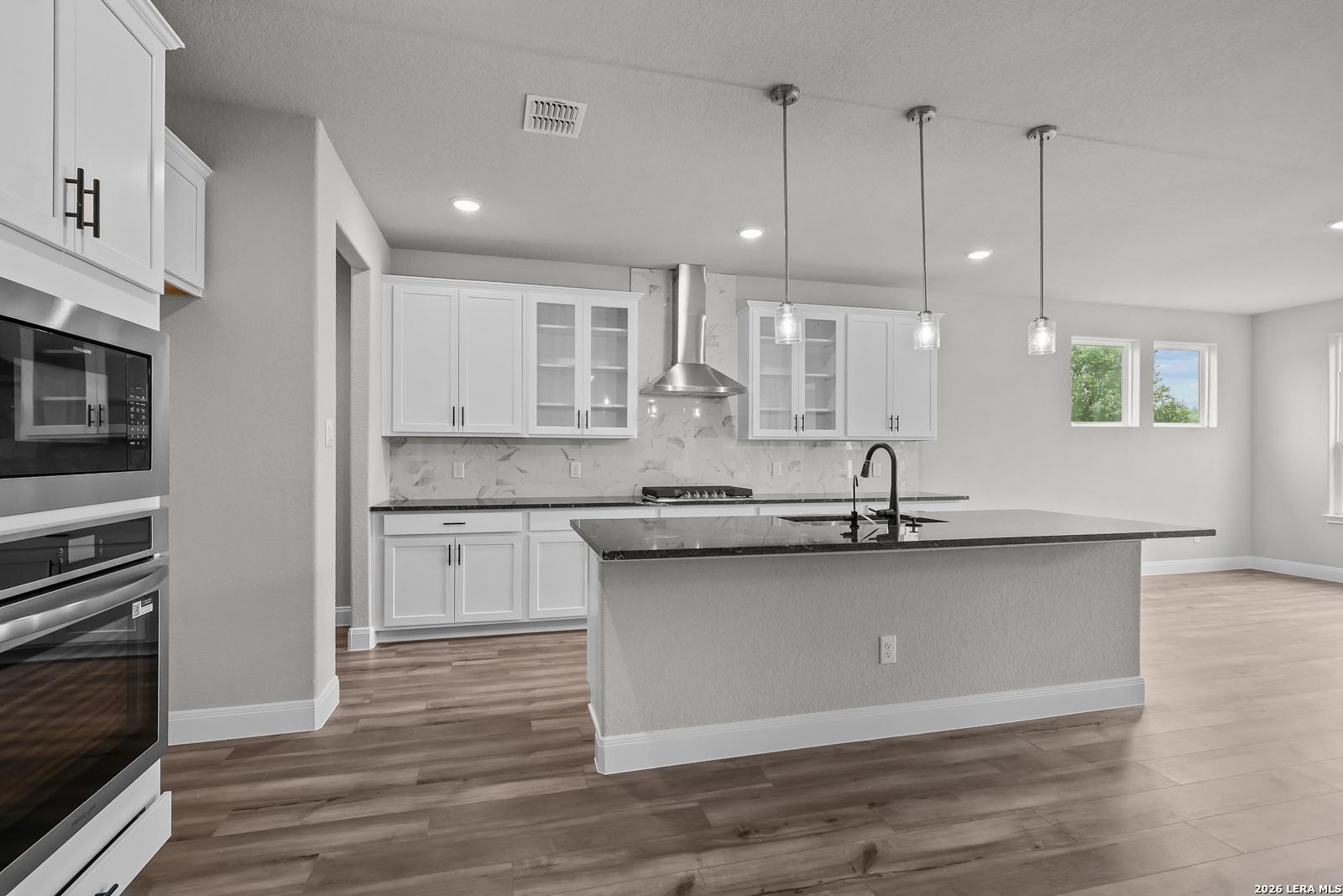 Modern white kitchen with stainless appliances, marble backsplash, granite island in Davidson Homes The Belmont H, Castroville, TX