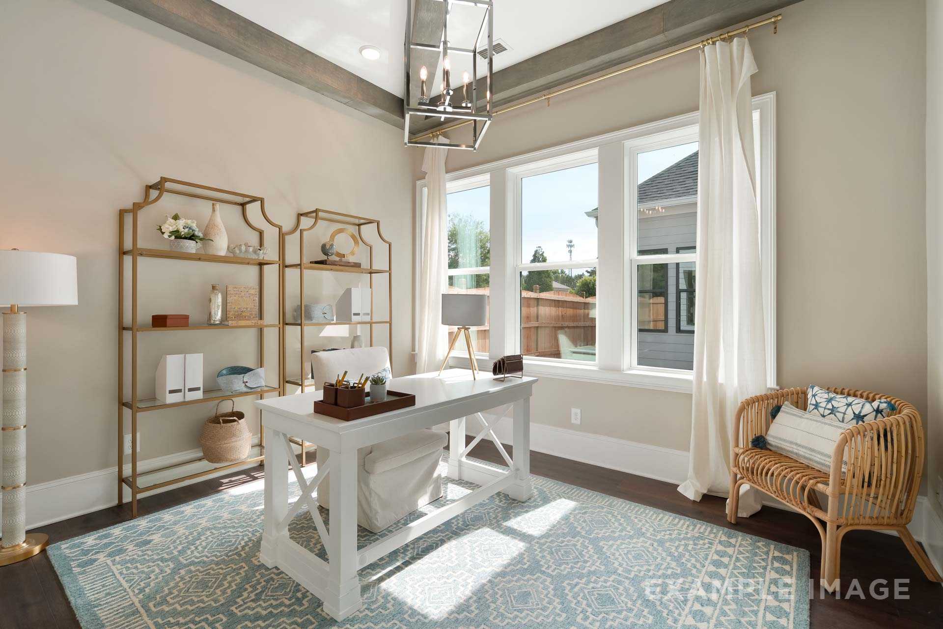 Spacious home office in The Seaside B with white farmhouse desk, gold bookshelves, woven chair, and sunlit windows