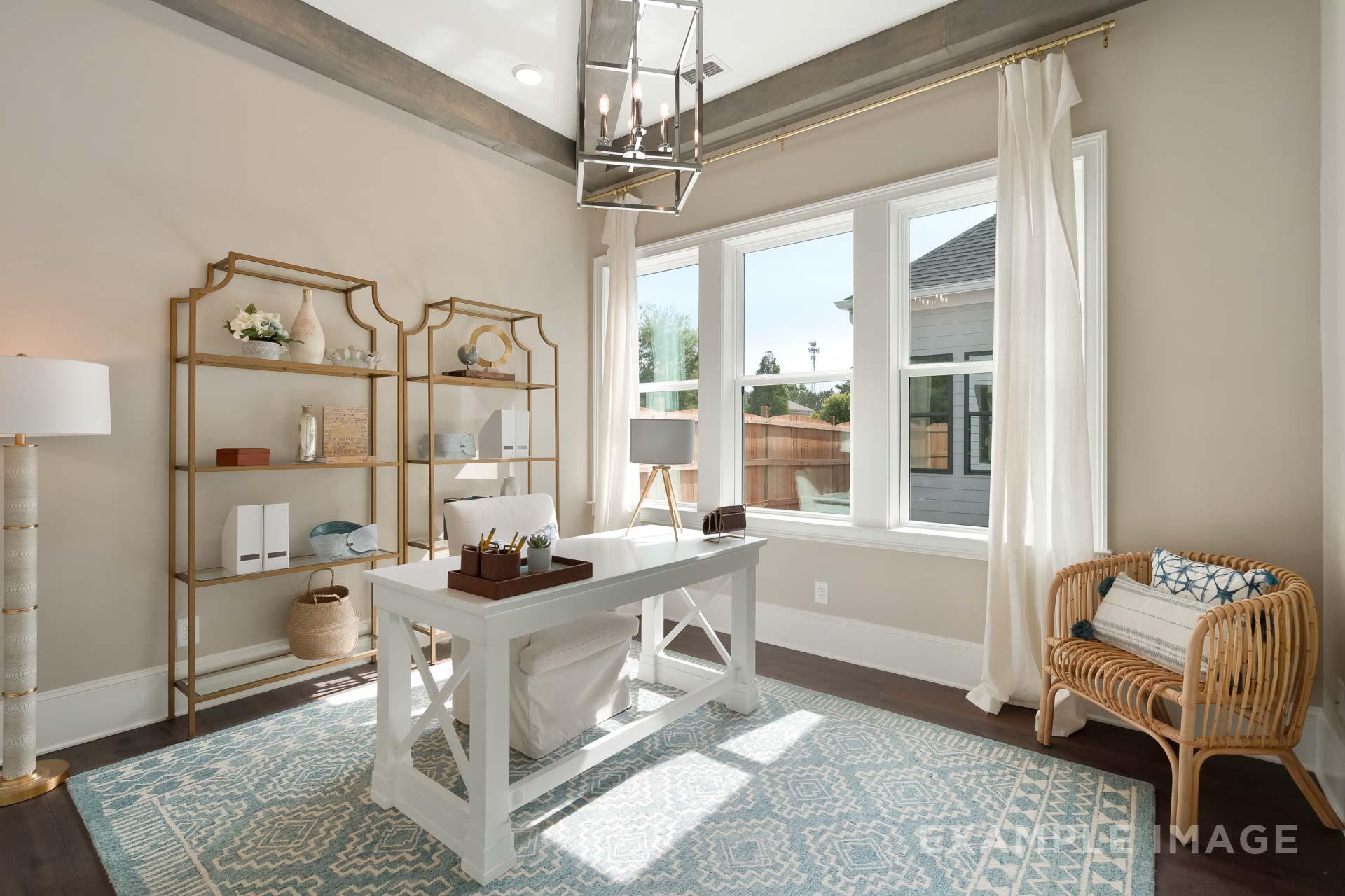 Spacious home office in The Seaside C featuring white farmhouse desk, gold metal shelves, wicker armchair, and sunlit windows
