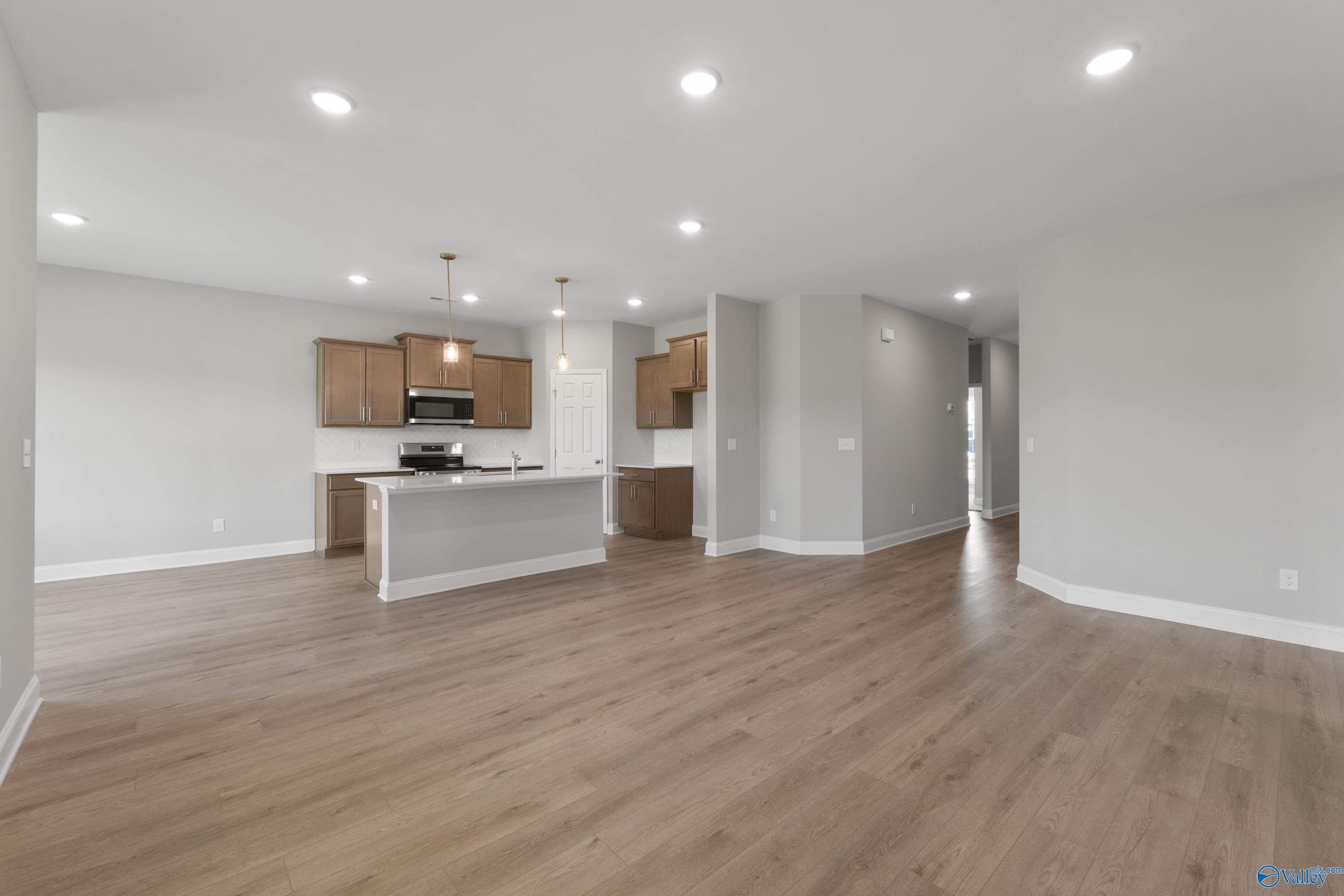 Modern open-concept kitchen with large island, pendant lights, and hardwood floors in The Asheville C by Davidson Homes, Athens, AL