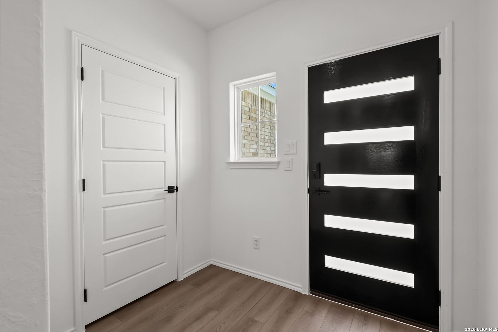 Bright entryway with modern black front door, frosted glass panels, and wood-look flooring in Davidson Homes' Pinecrest F, San Antonio
