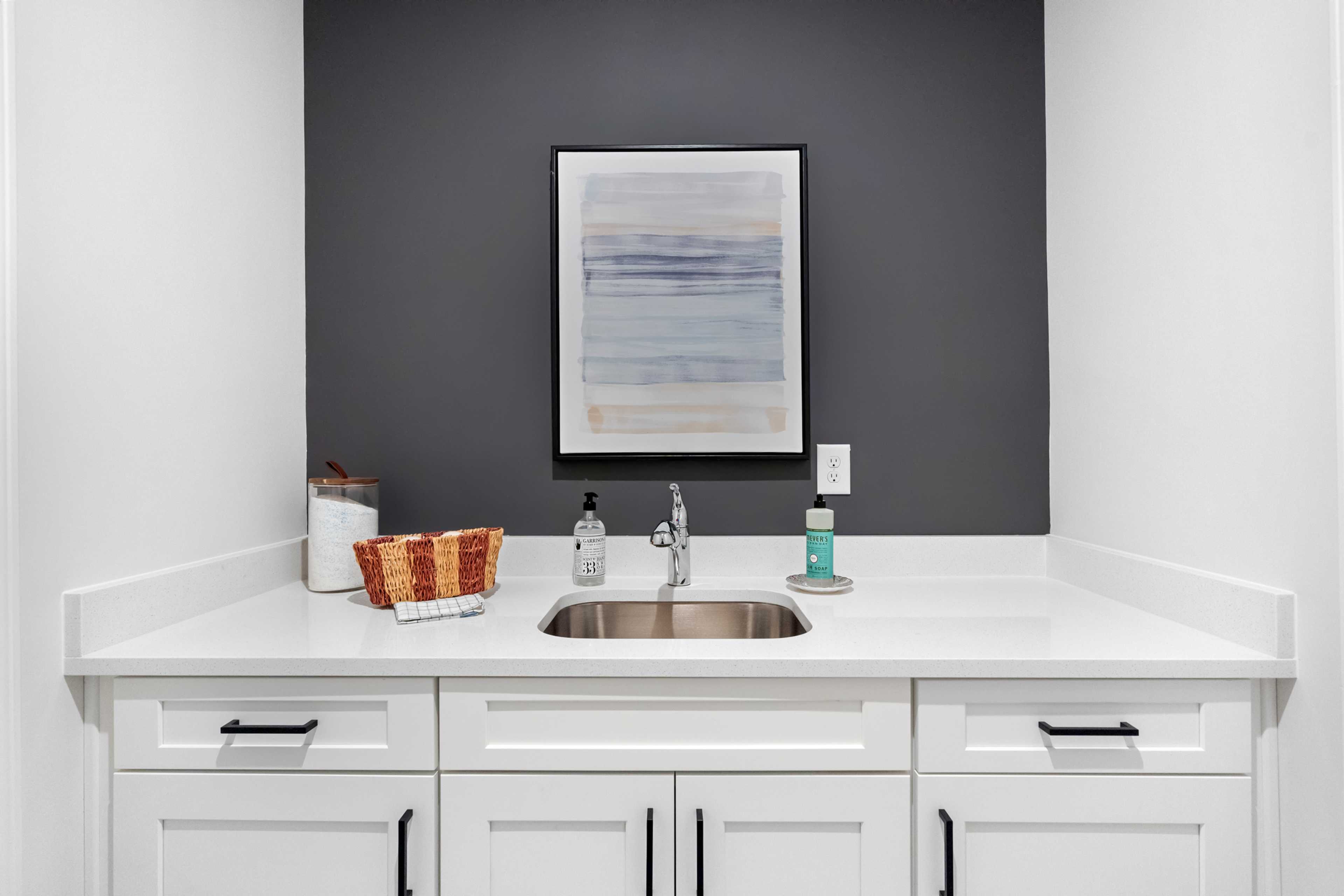 Modern utility sink area at Kelly Preserve in Loganville Georgia with white shaker cabinets, stainless sink and abstract wall art