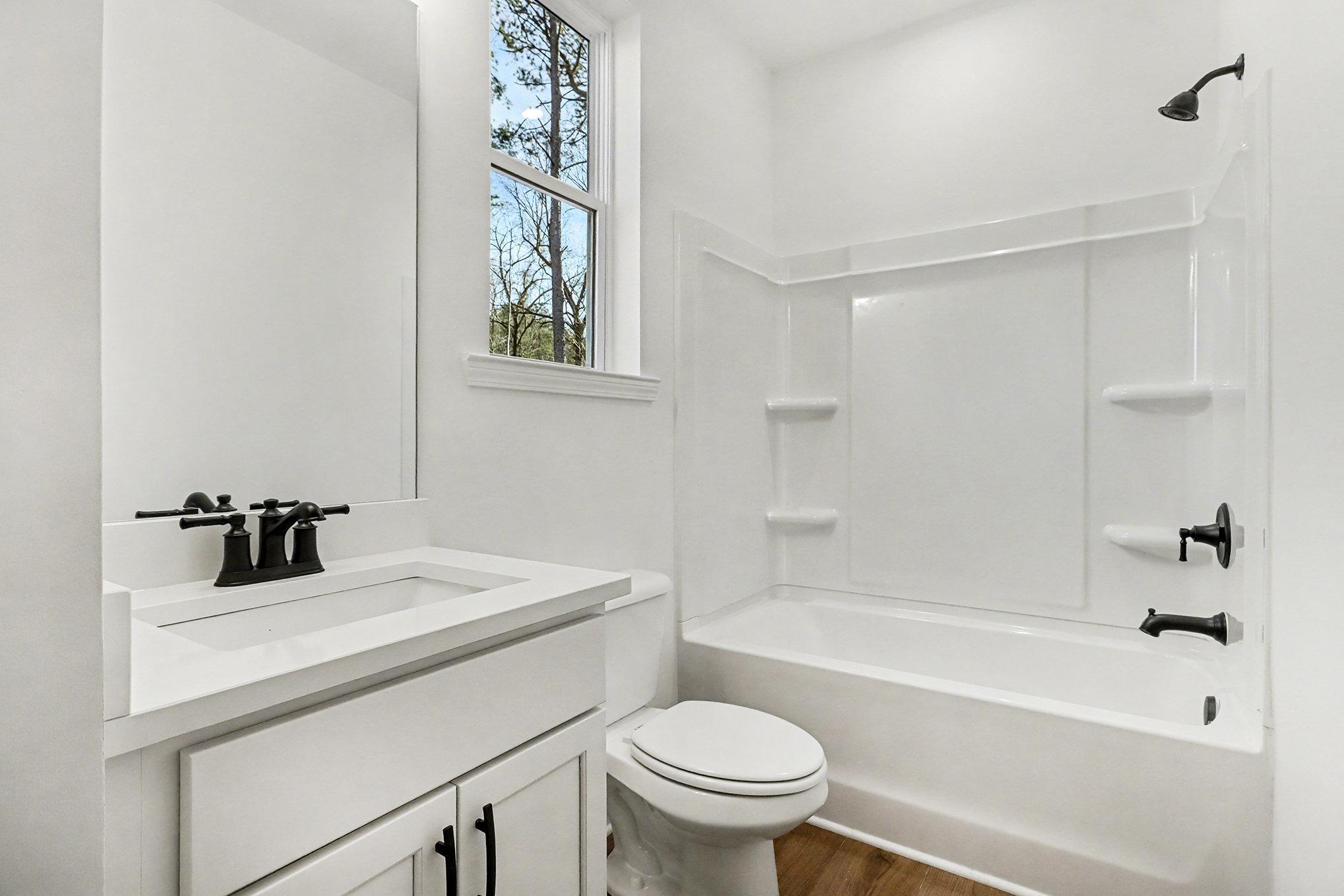 Bright bathroom with white vanity, single sink, soaking tub-shower combo, and toilet in Davidson Homes The Daphne B, Loganville, GA