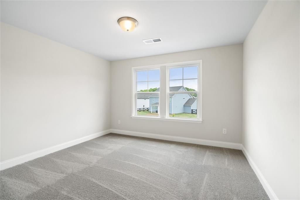 Bright secondary bedroom with large windows overlooking backyard and beige carpet in Davidson Homes The Willow B, Hoschton, Georgia