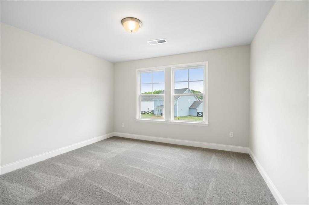 Bright secondary bedroom with large windows overlooking backyard and beige carpet in Davidson Homes The Willow B, Hoschton, Georgia