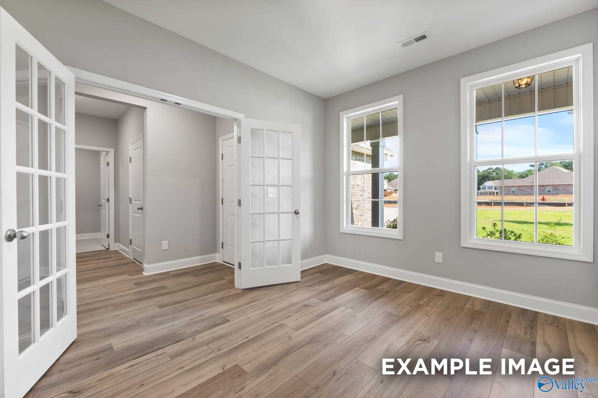 Bright living room with gray walls, hardwood floors, French doors, and large windows overlooking yard in The Rockford D, Hazel Green, AL