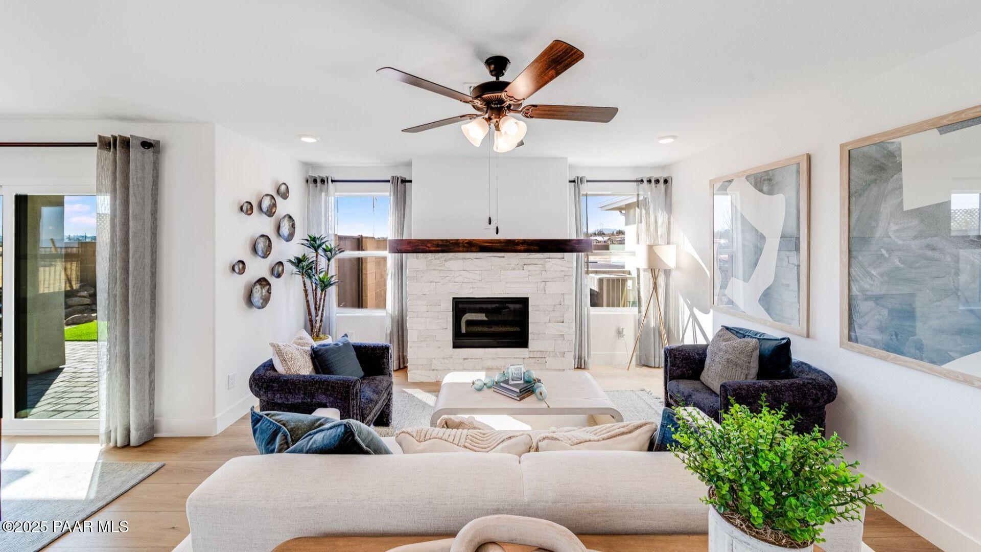 Cozy living room with white stone fireplace, ceiling fans, plush sofa, and sliding doors to lush patio in Davidson Homes The Wilmington B, Prescott, Arizona