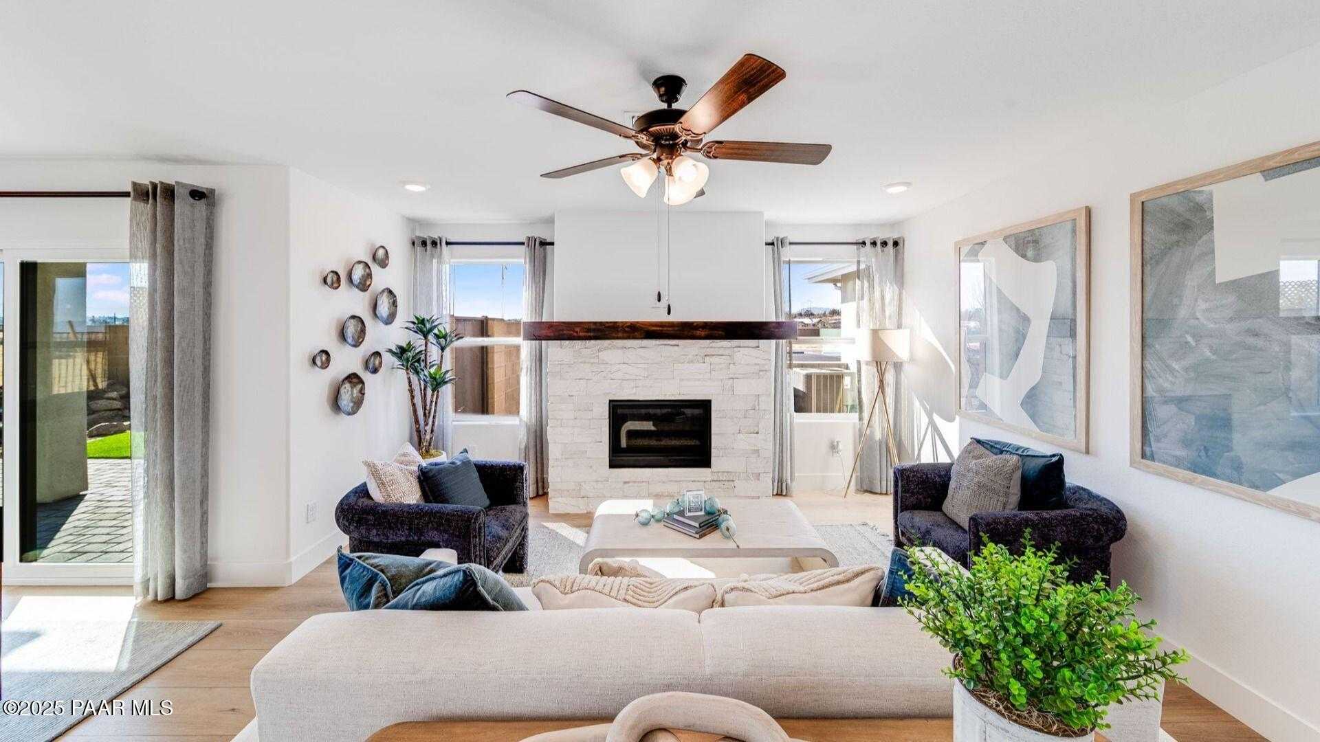 Cozy living room with white stone fireplace, ceiling fans, plush sofa, and sliding doors to lush patio in Davidson Homes The Wilmington B, Prescott, Arizona