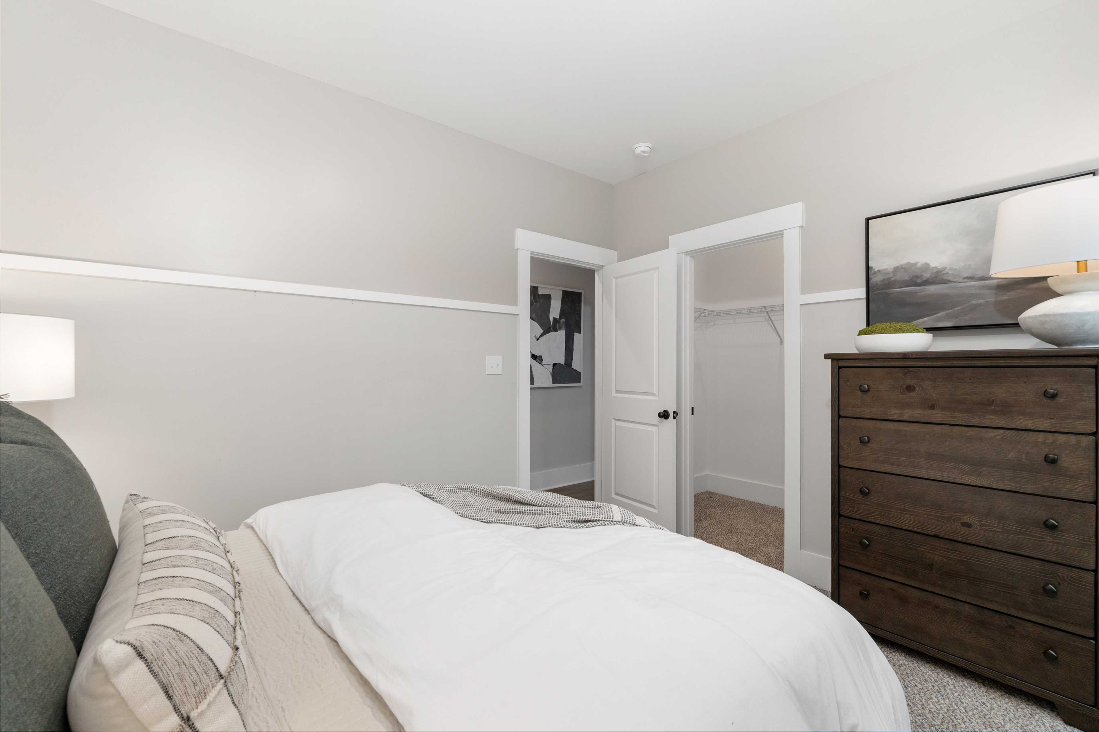 Cozy bedroom interior at Kendall Farms in Toney Alabama with queen bed neutral bedding wooden dresser and open walk-in closet