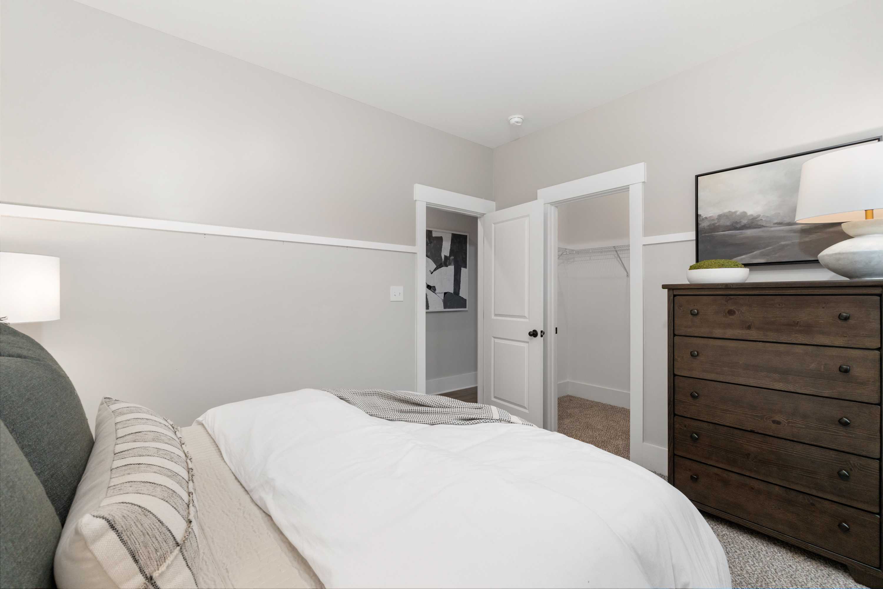 Cozy bedroom interior at Kendall Farms in Toney Alabama with queen bed neutral bedding wooden dresser and open walk-in closet