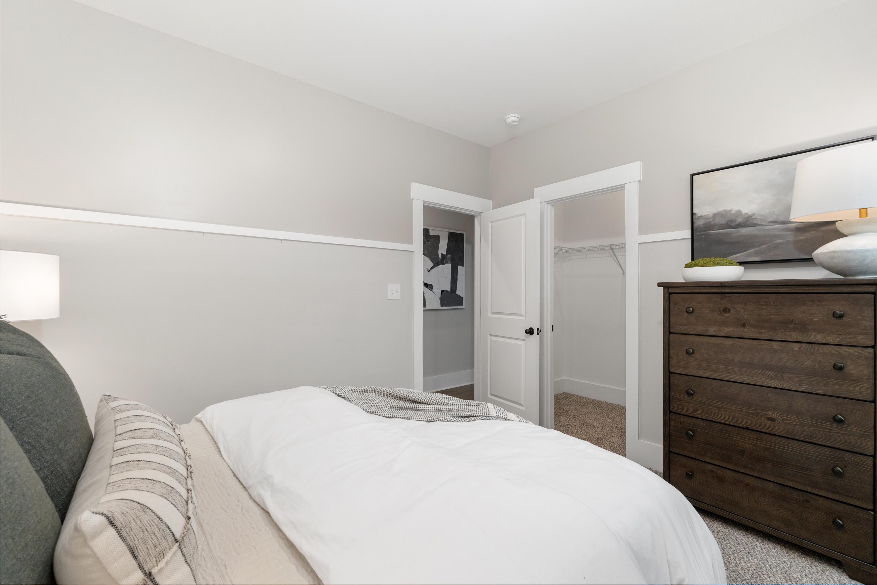 Cozy bedroom interior at Kendall Farms in Toney Alabama with queen bed neutral bedding wooden dresser and open walk-in closet