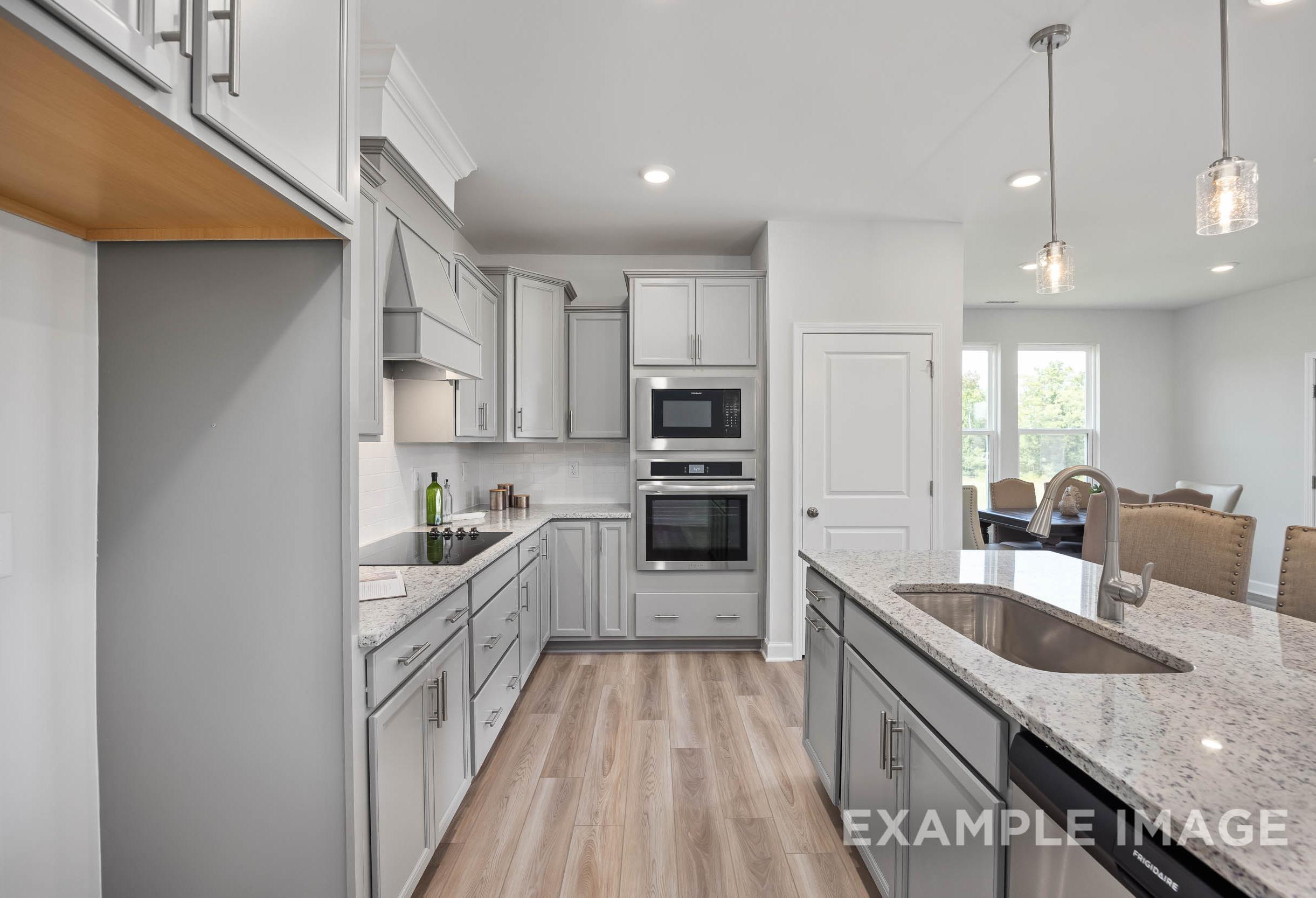 Modern kitchen in The Daphne C with white shaker cabinets, large granite island sink, double ovens, and open dining nook