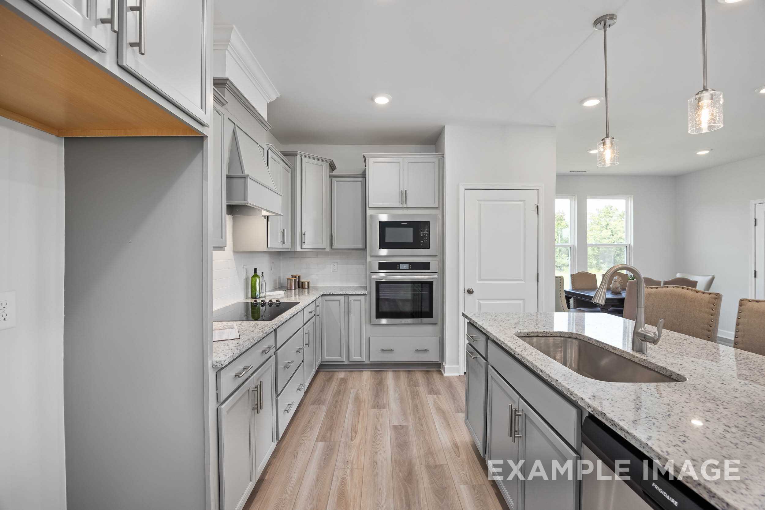 Modern kitchen in The Daphne C with white shaker cabinets, large granite island sink, double ovens, and open dining nook