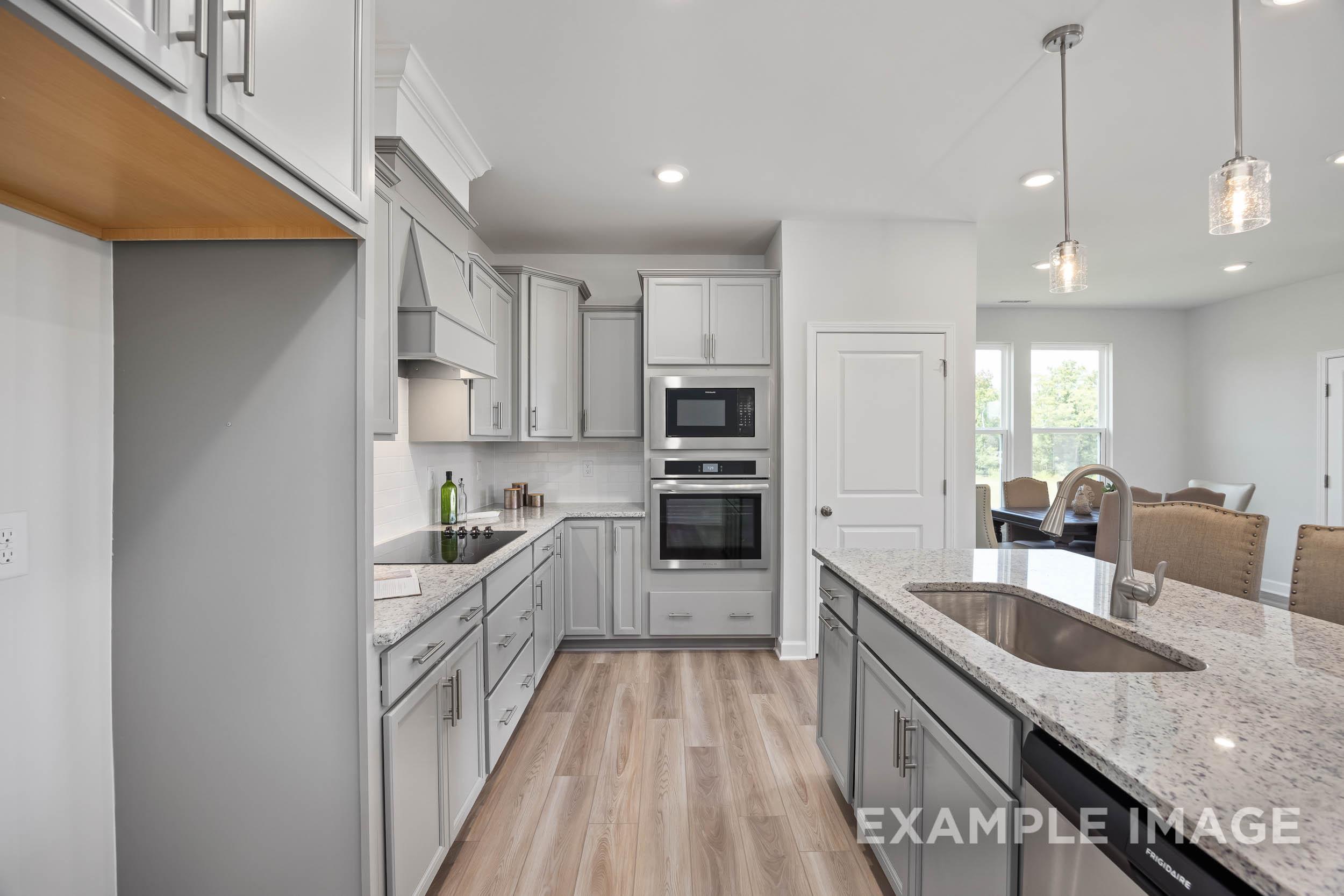 Modern kitchen in The Daphne C with white shaker cabinets, large granite island sink, double ovens, and open dining nook