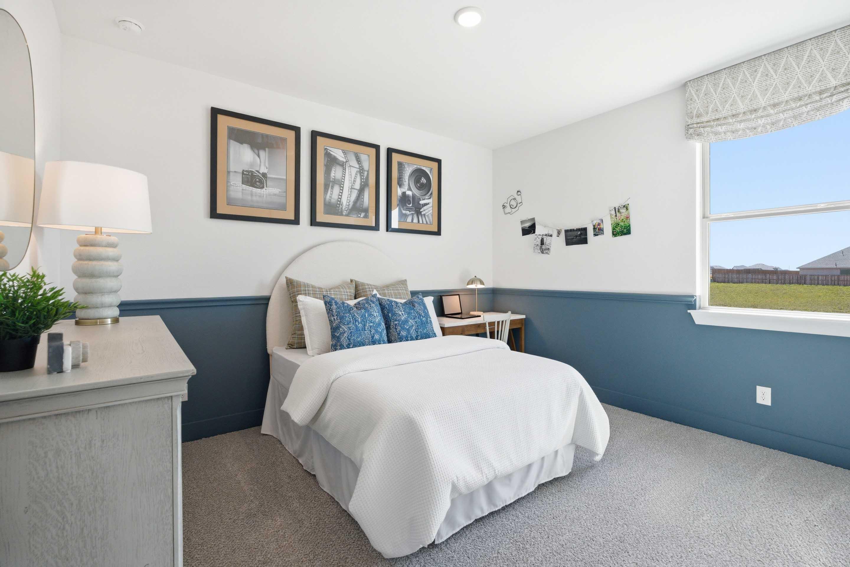 Bright, modern secondary bedroom in The Laurel M home design featuring blue wainscoting and a cozy workspace.