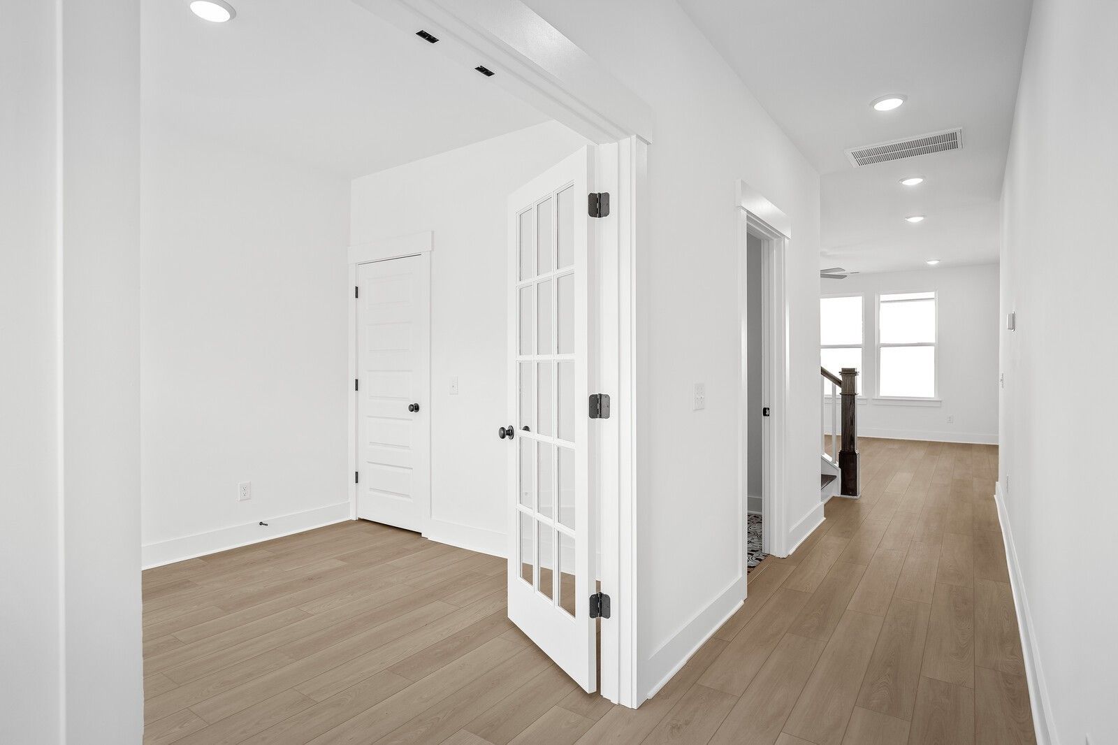 Bright upstairs hallway with open glass-panel doors, hardwood floors, and staircase in The Logan C by Davidson Homes, Gallatin, TN