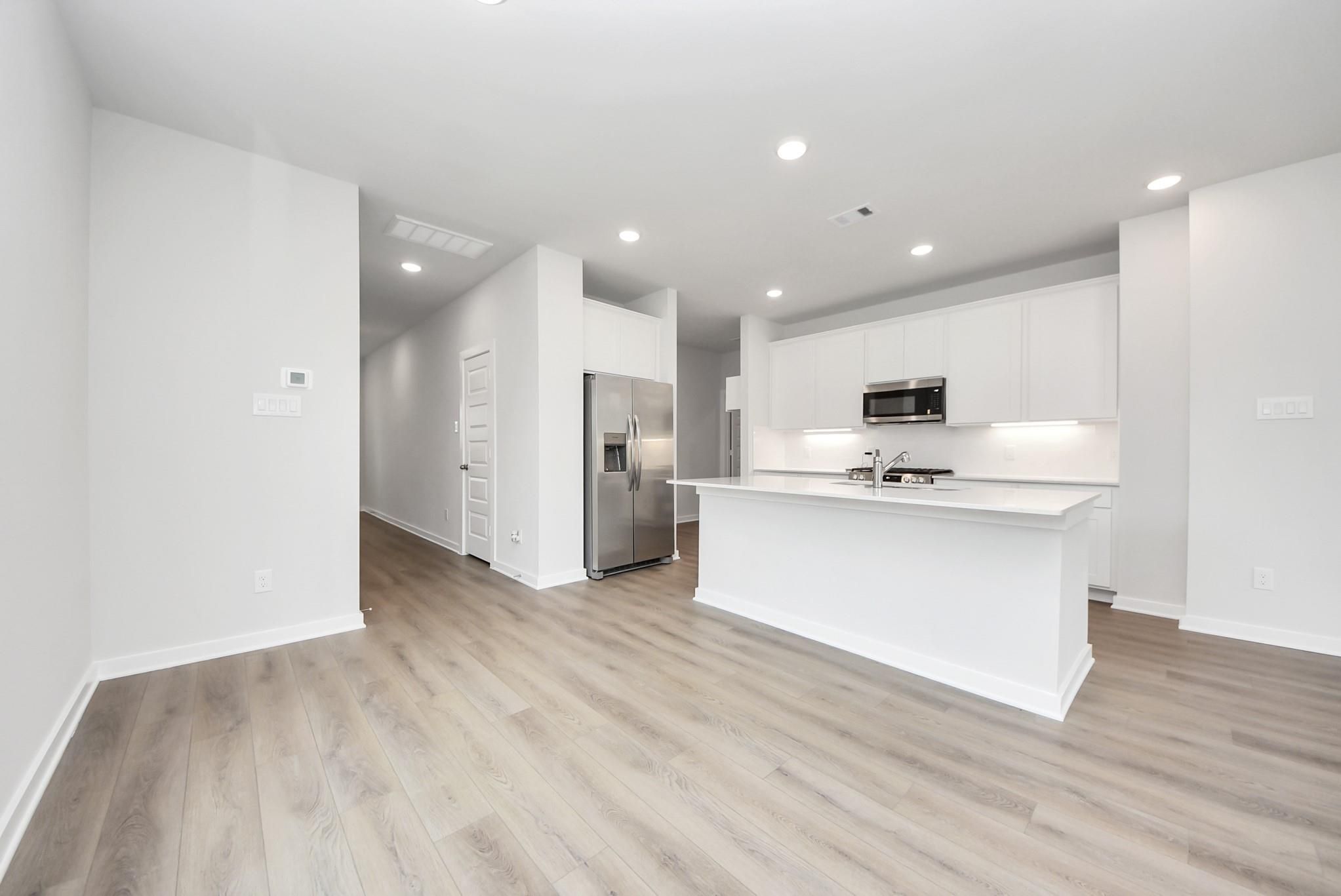 Modern kitchen with white cabinets, island, and stainless steel appliances in The Blanco E floor plan, Dayton, Texas.