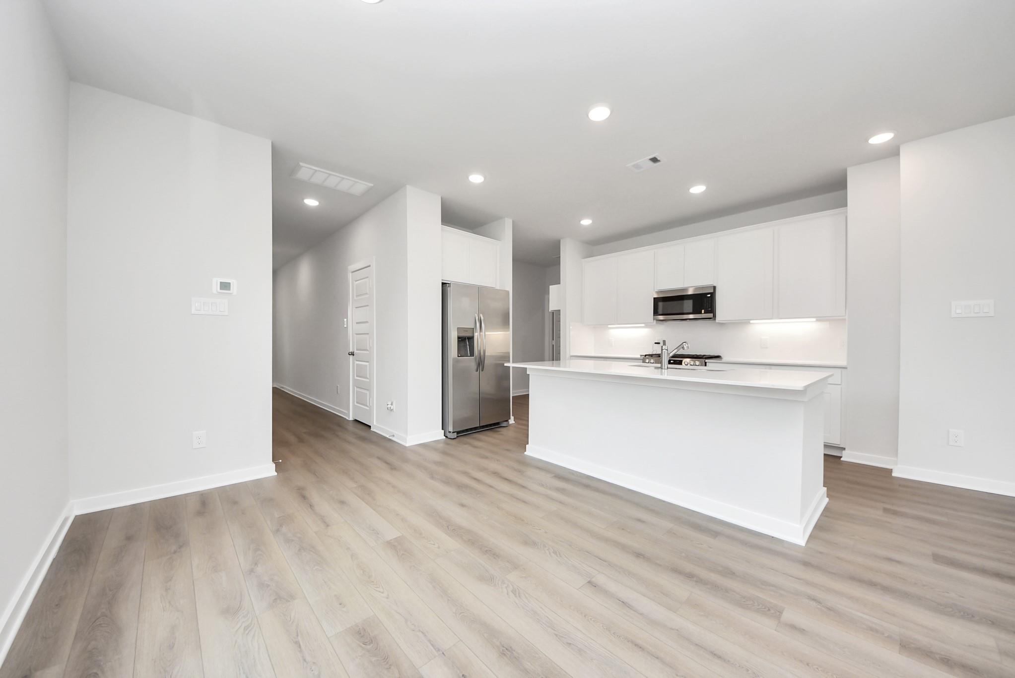 Modern kitchen with white cabinets, island, and stainless steel appliances in The Blanco E floor plan, Dayton, Texas.