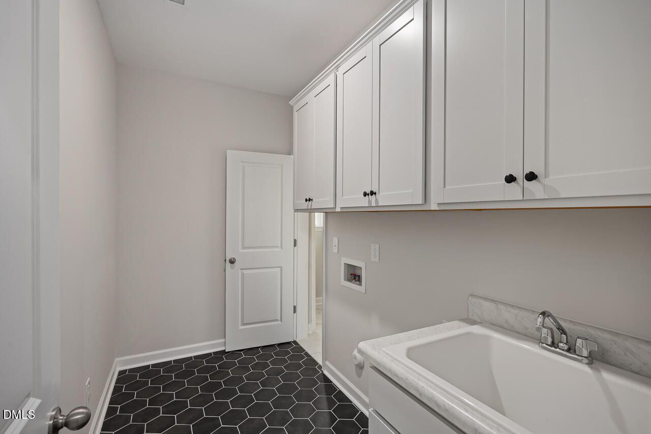 Laundry room with white cabinets, utility sink, and hexagonal tile flooring in The Ashport L at Sage on North Main.