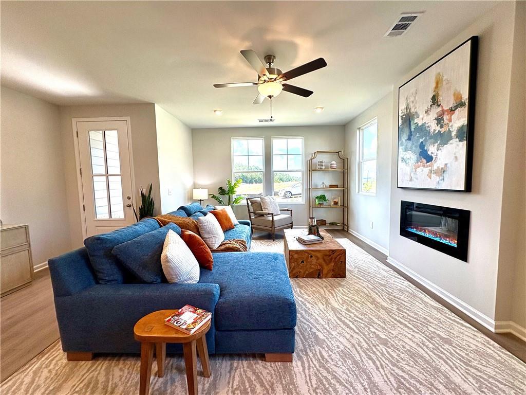 Cozy living room with navy L-shaped sectional, wooden coffee table, electric fireplace, and abstract wall art in Davidson Homes The Monroe A, Emerson, GA