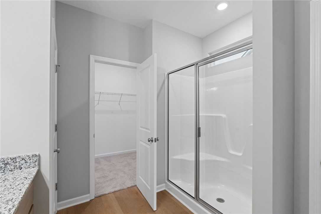 Modern master bathroom with frameless glass shower, granite vanity, and walk-in closet in Davidson Homes The Luna B, Opelika