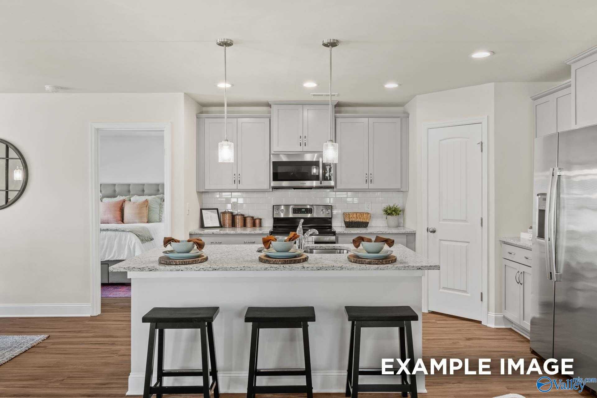 Open-concept kitchen with white shaker cabinets, stainless steel appliances, and island bar overlooking master bedroom in Davidson Homes The Franklin C, New Market, Alabama