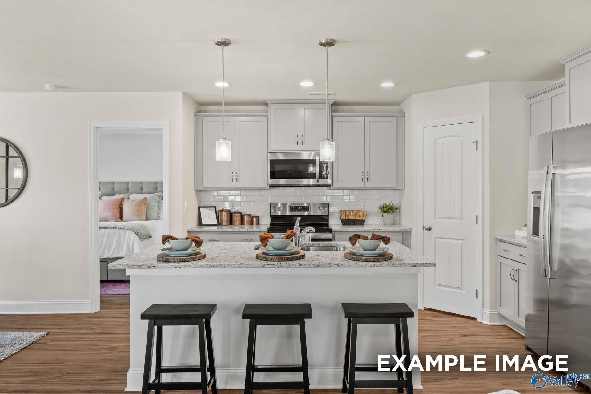 Modern white kitchen with stainless appliances, island bar stools, and open bedroom view in Davidson Homes Franklin C, Hazel Green, AL