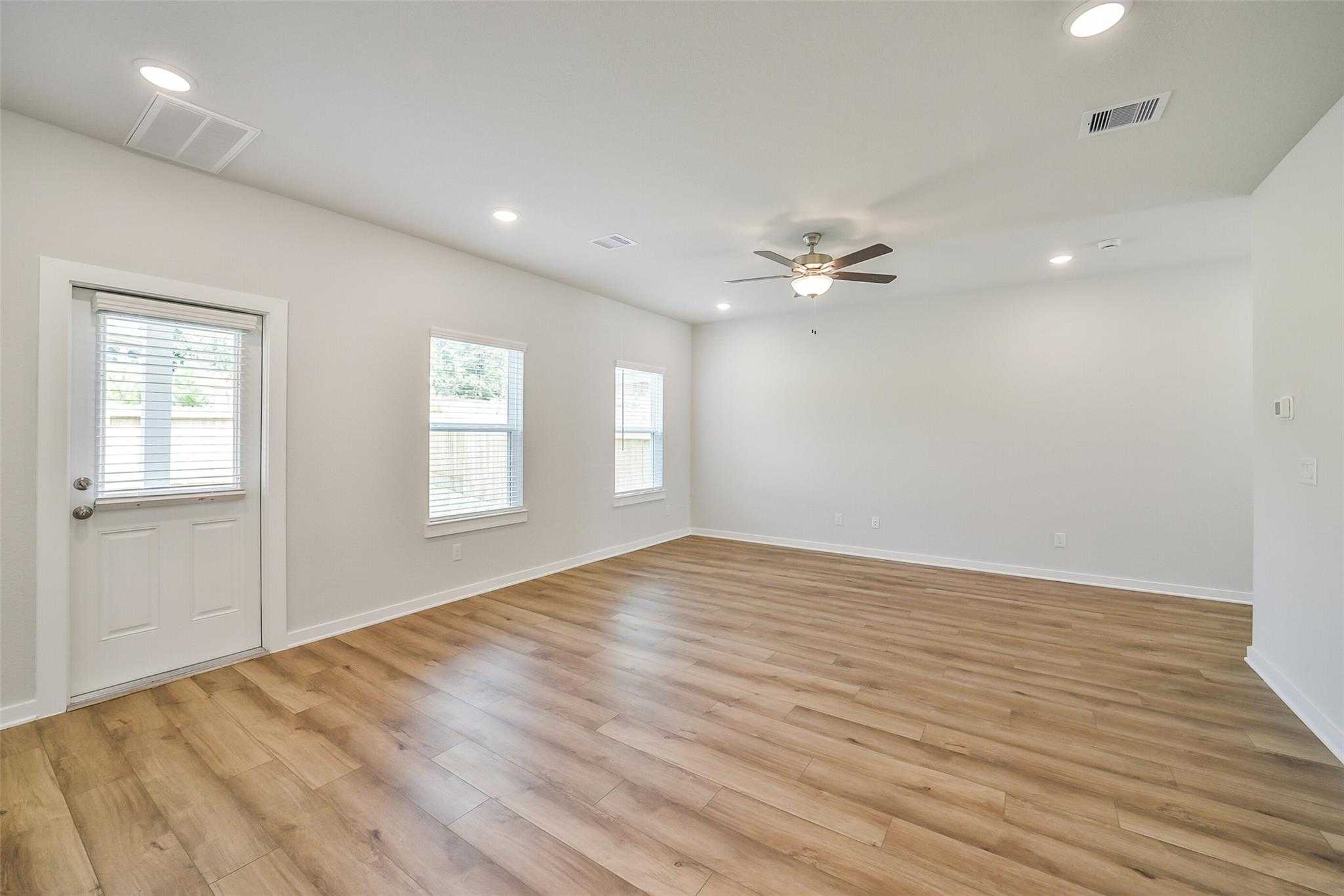 Bright living room with hardwood floors, ceiling fans, and large windows in Davidson Homes The Trinity F, Magnolia, Texas