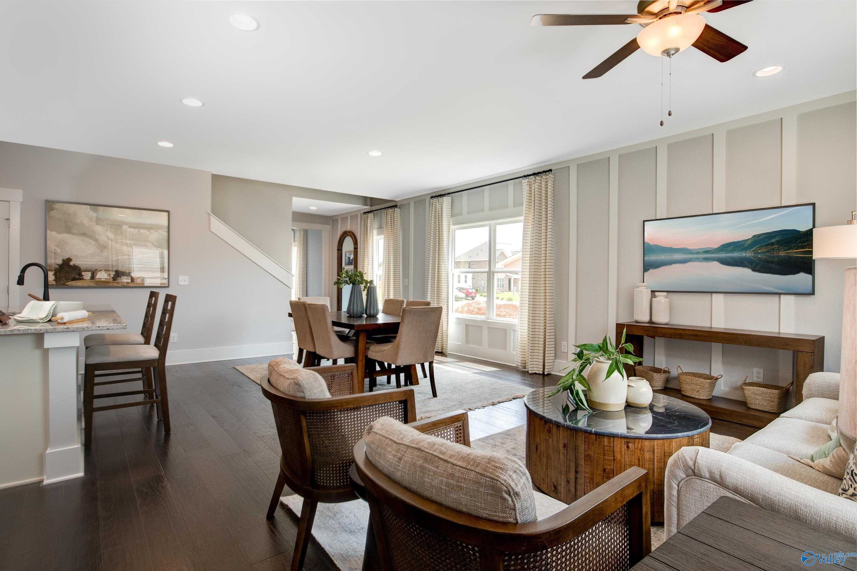Open-concept living and dining area with wooden table, beige sofa, ceiling fan, and large windows in Davidson Homes The Covington C, Decatur, Alabama