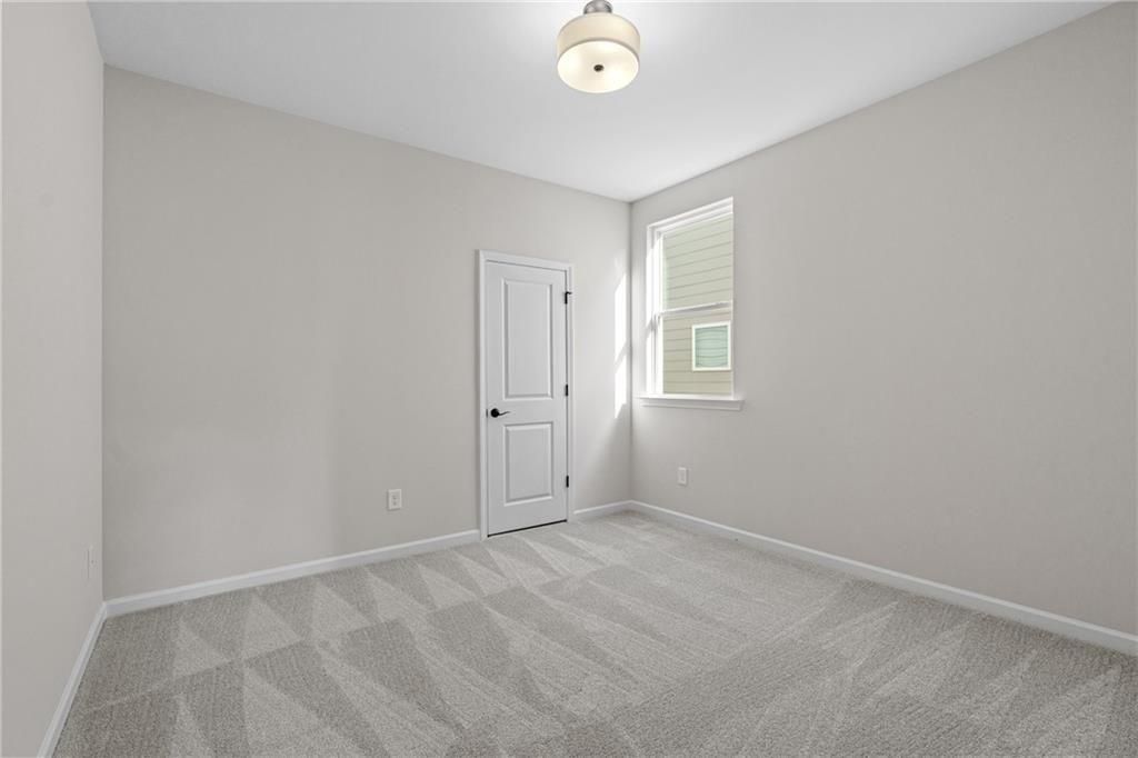 Empty secondary bedroom featuring gray walls, patterned carpet, white door, and window in Davidson Homes The Edison A, Loganville, GA