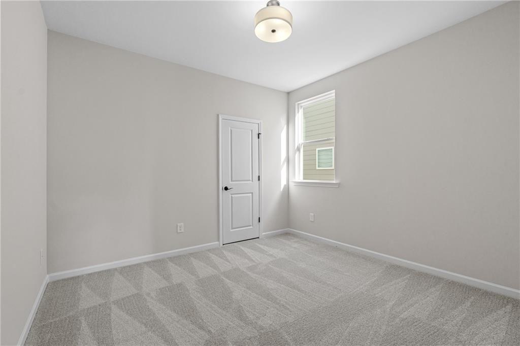Empty secondary bedroom featuring gray walls, patterned carpet, white door, and window in Davidson Homes The Edison A, Loganville, GA